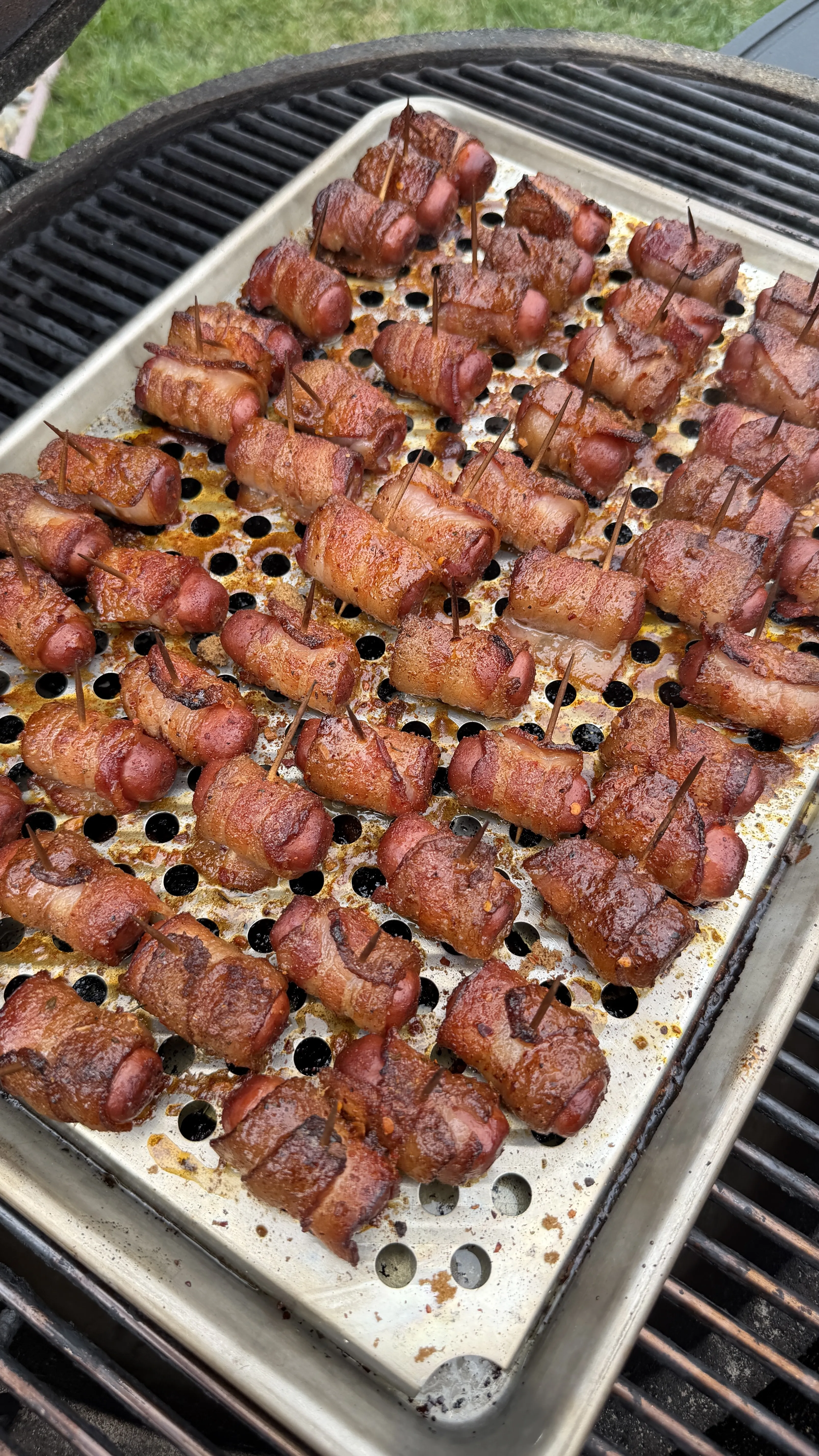 Cajun honey bacon-wrapped little smokies secured with toothpicks on a perforated grill pan over charcoal grill