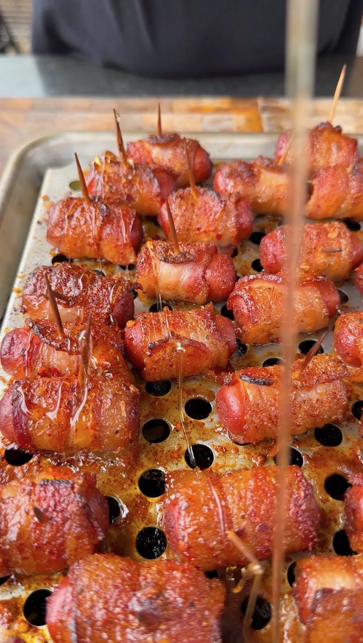 Glazed Cajun honey bacon-wrapped little smokies secured with toothpicks on a perforated baking sheet