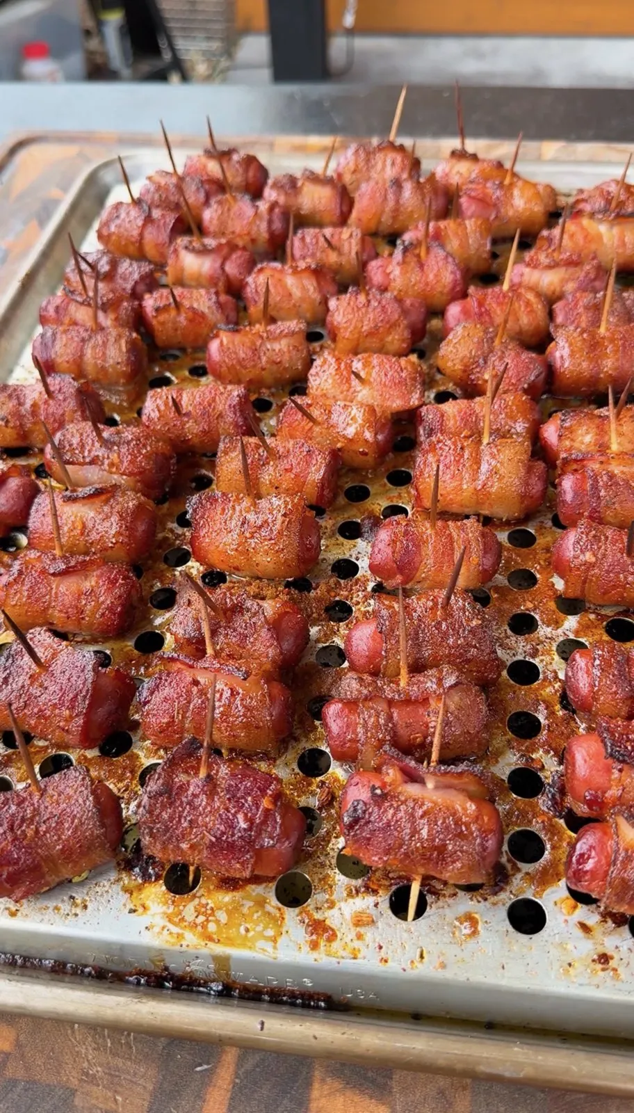Cajun honey bacon-wrapped little smokies on a perforated sheet pan, secured with toothpicks, caramelized and golden brown