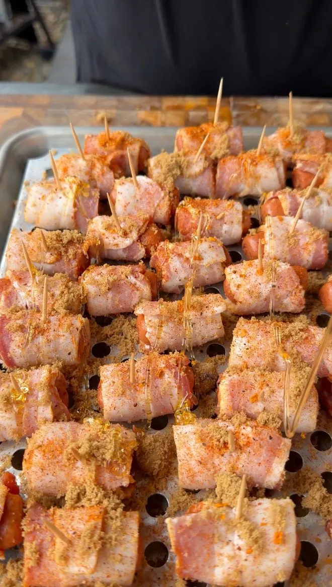 Raw bacon-wrapped little smokies on a baking tray, topped with brown sugar and Cajun seasoning, secured with toothpicks