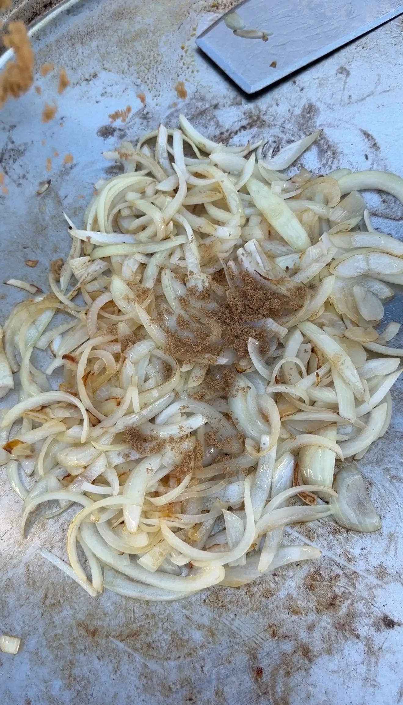 Sliced onions cooking on a flat top griddle with brown seasoning, partially caramelized for croissant burgers
