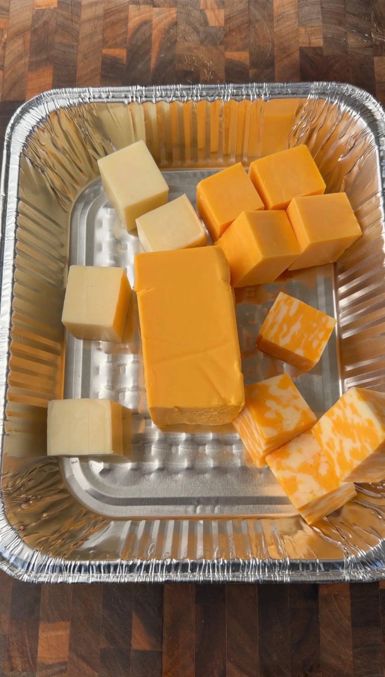 Assorted cheddar and white cheese cubes in a disposable aluminum pan for smoked queso dip