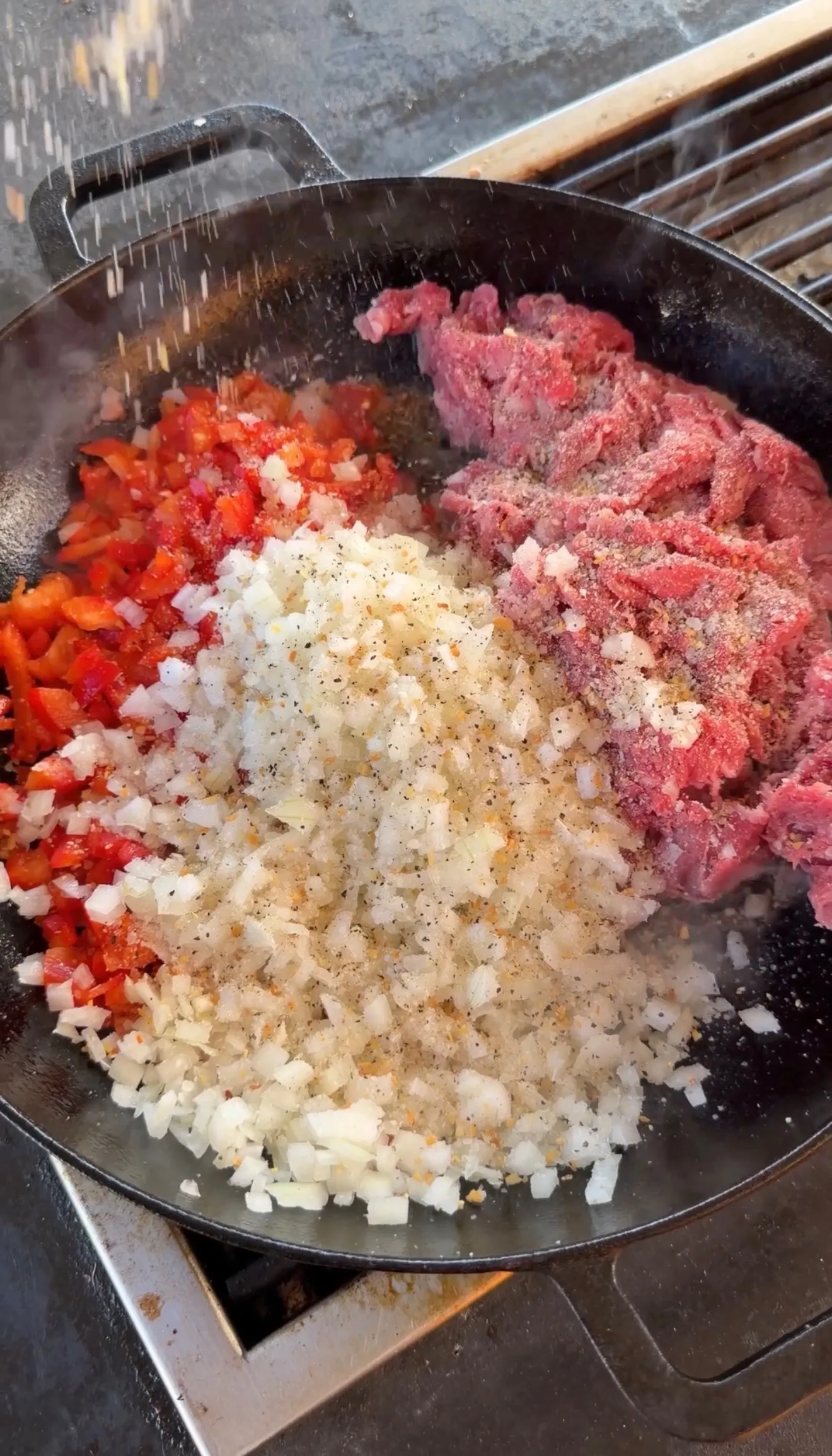 Raw sliced beef, diced onions, and red peppers with seasoning in a cast iron skillet for cheesesteak stuffed pockets