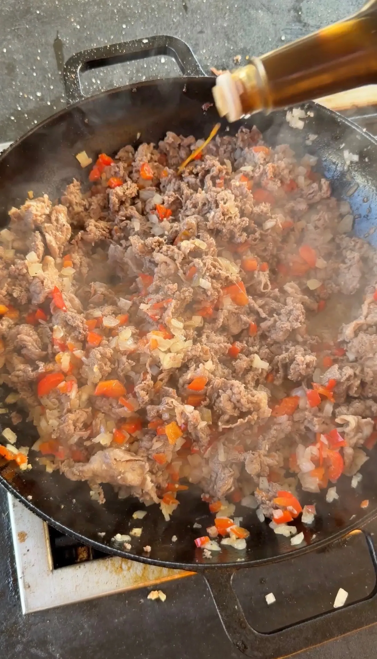 Ground beef with diced red peppers and onions sizzling in a cast iron skillet for cheesesteak stuffed pockets