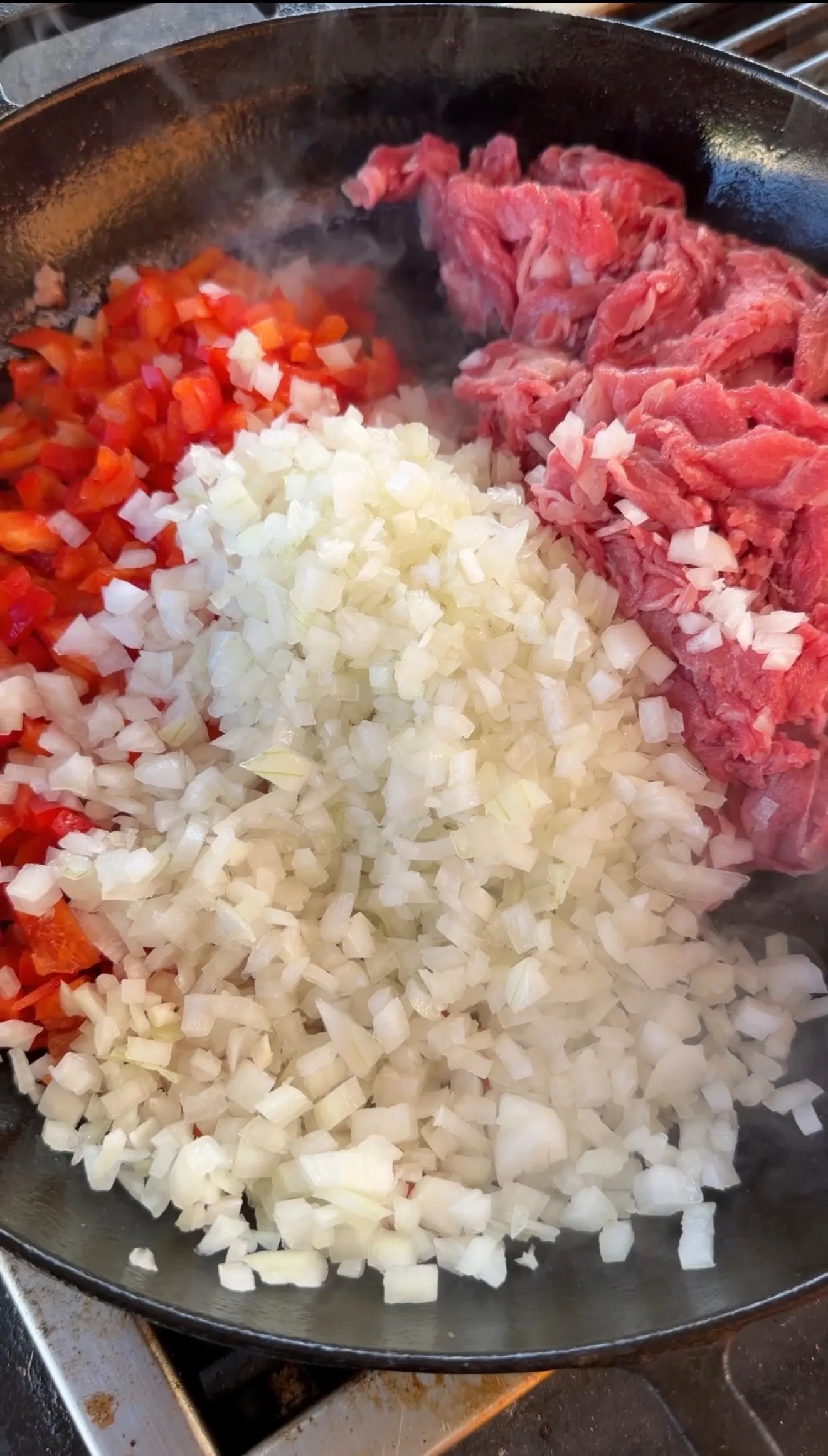 Raw sliced beef, diced white onions, and chopped red bell peppers in a cast iron skillet for cheesesteak stuffed pockets