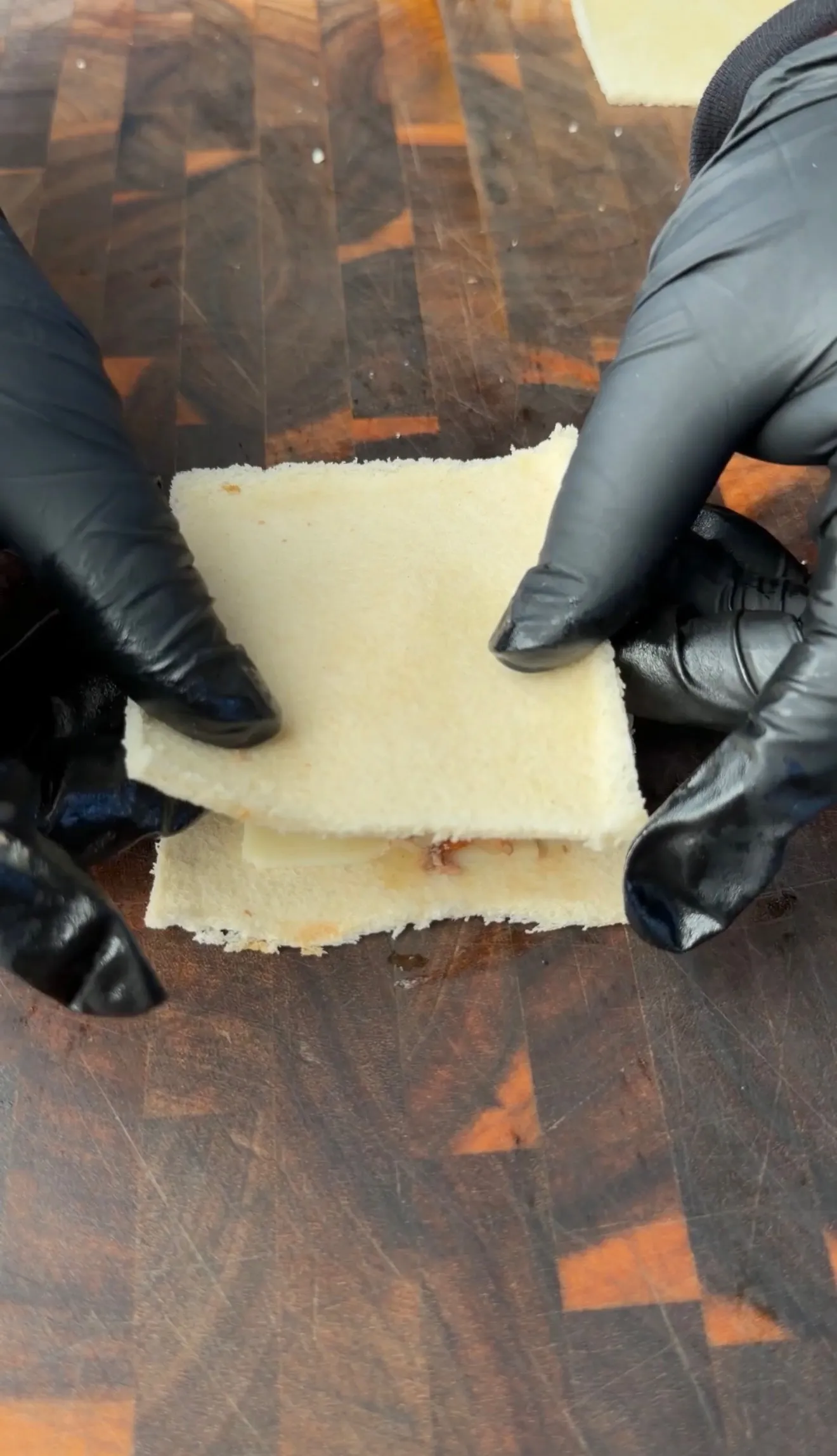 Gloved hands assembling a cheesesteak stuffed bread pocket on a wooden cutting board