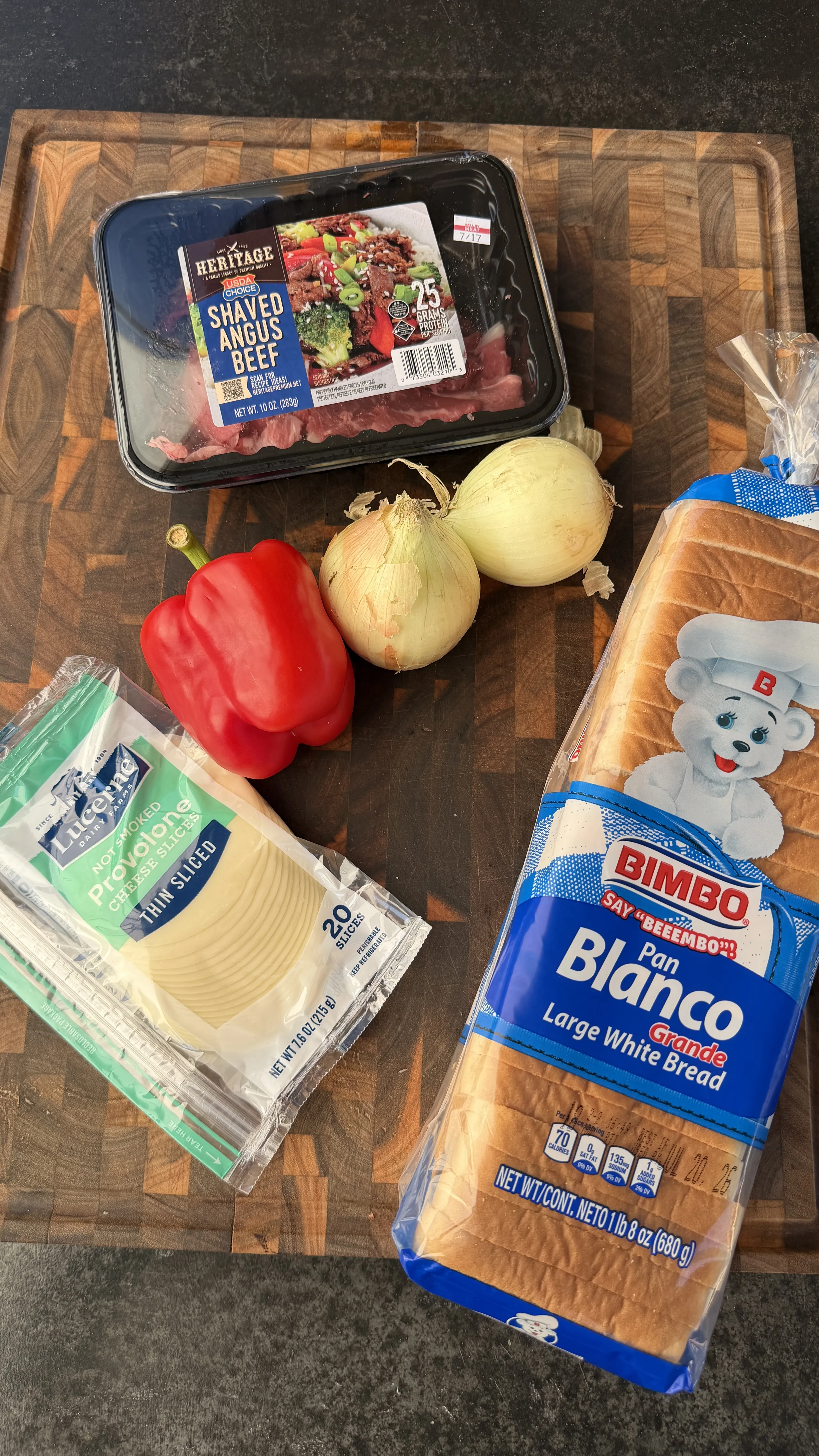 Cheesesteak pocket ingredients including shaved beef, provolone, bell pepper, onion, and white bread on a cutting board