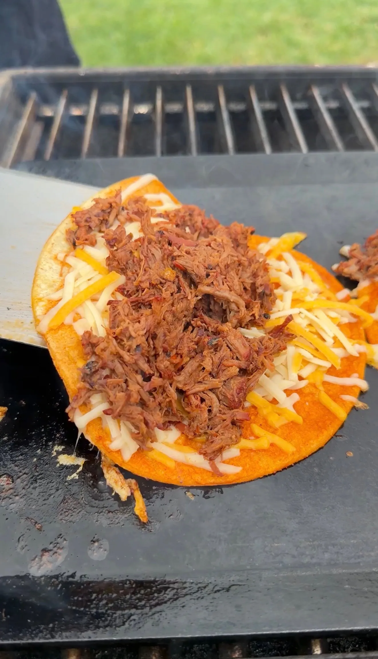Cheesy birria taco on a flat top griddle topped with shredded beef and melted cheese blend