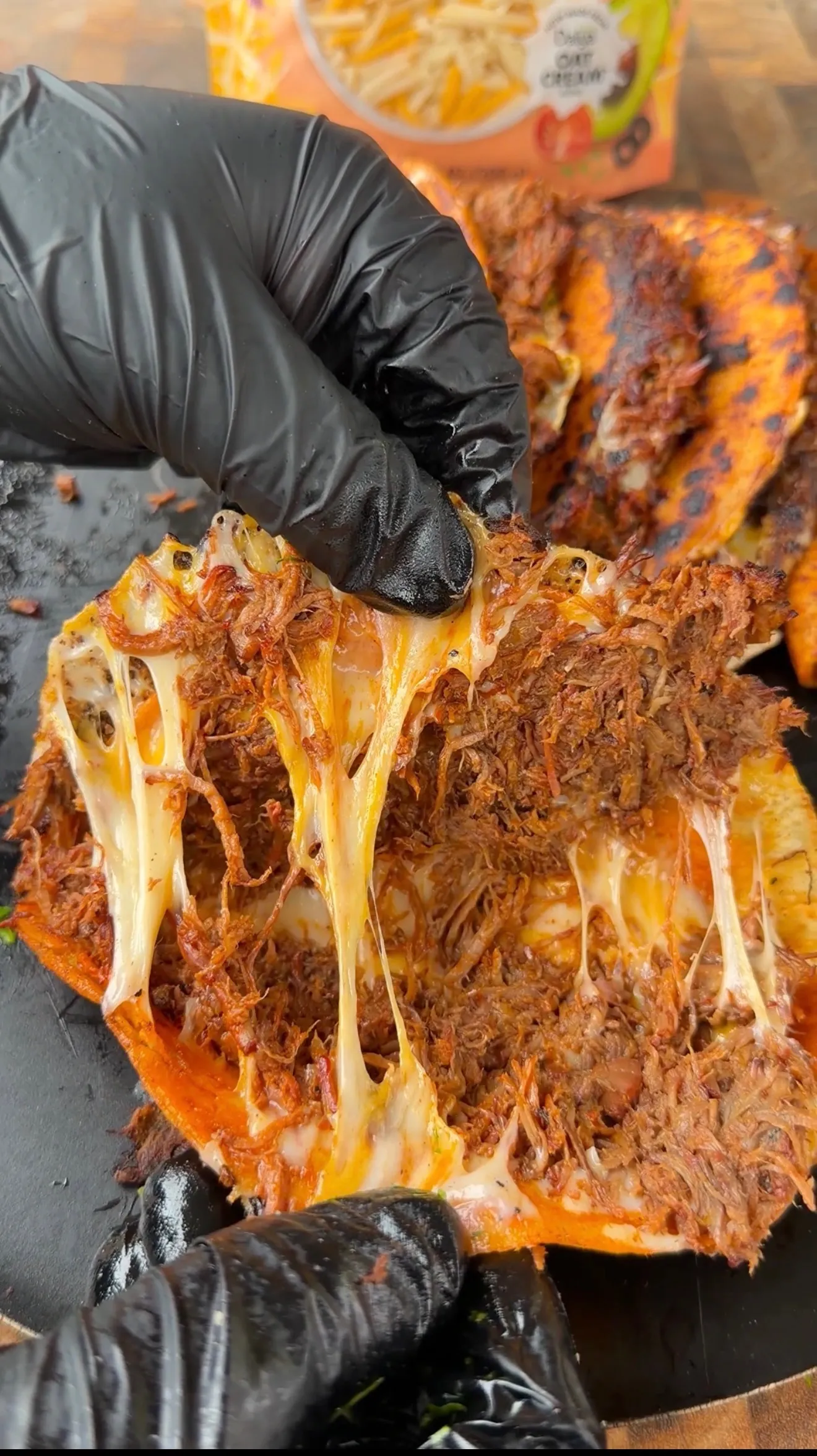 Gloved hands pulling apart cheesy birria tacos with dramatic melted cheese strings and shredded meat