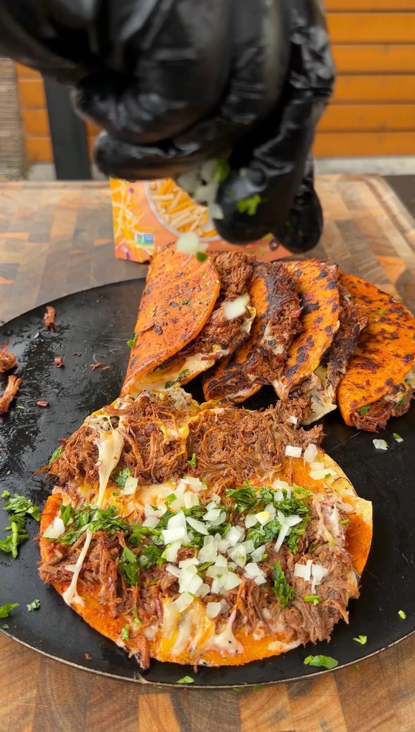 Cheesy birria tacos on a hot comal topped with chopped cilantro and diced white onion, filled with shredded beef
