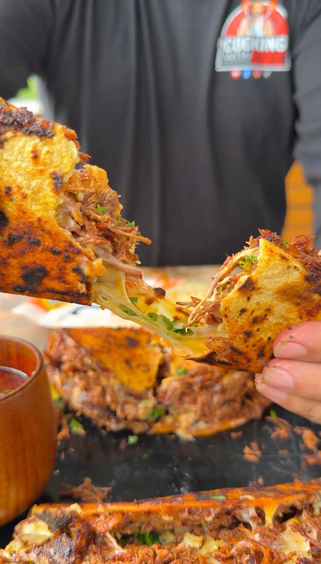Crispy birria tacos being pulled apart revealing melted cheese and shredded beef, served with consomé dipping sauce