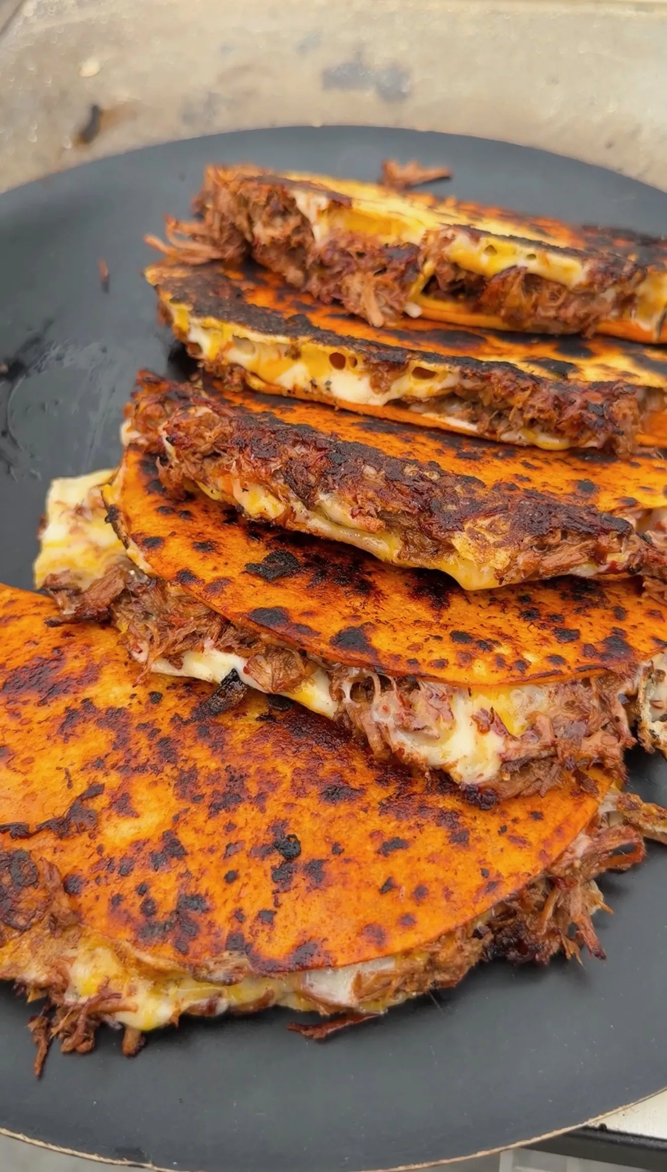 Crispy birria quesatacos stacked on a dark griddle, filled with shredded beef and melted cheese