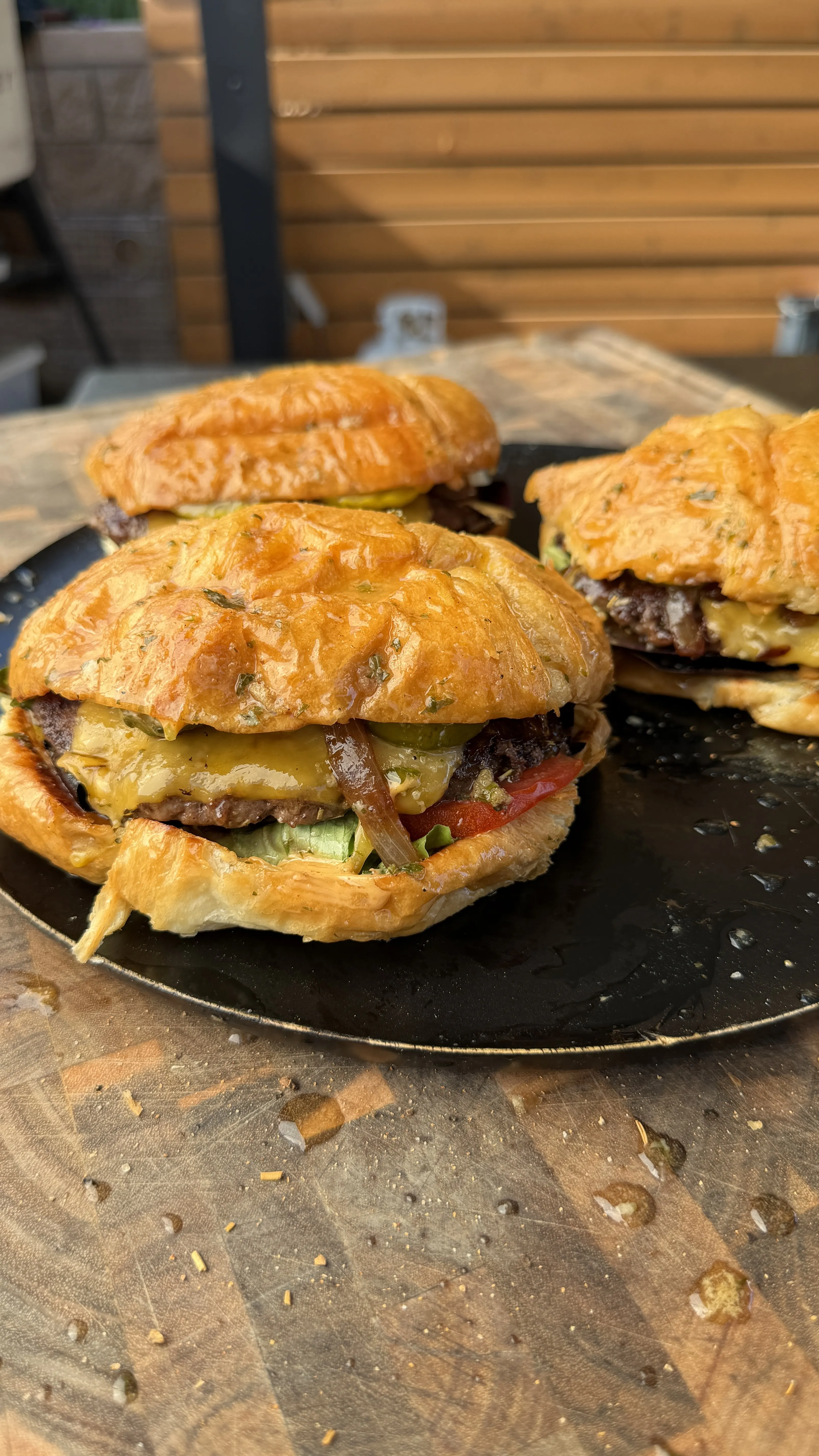 Juicy croissant burgers with melted cheese, tomato, and caramelized onions on a dark plate