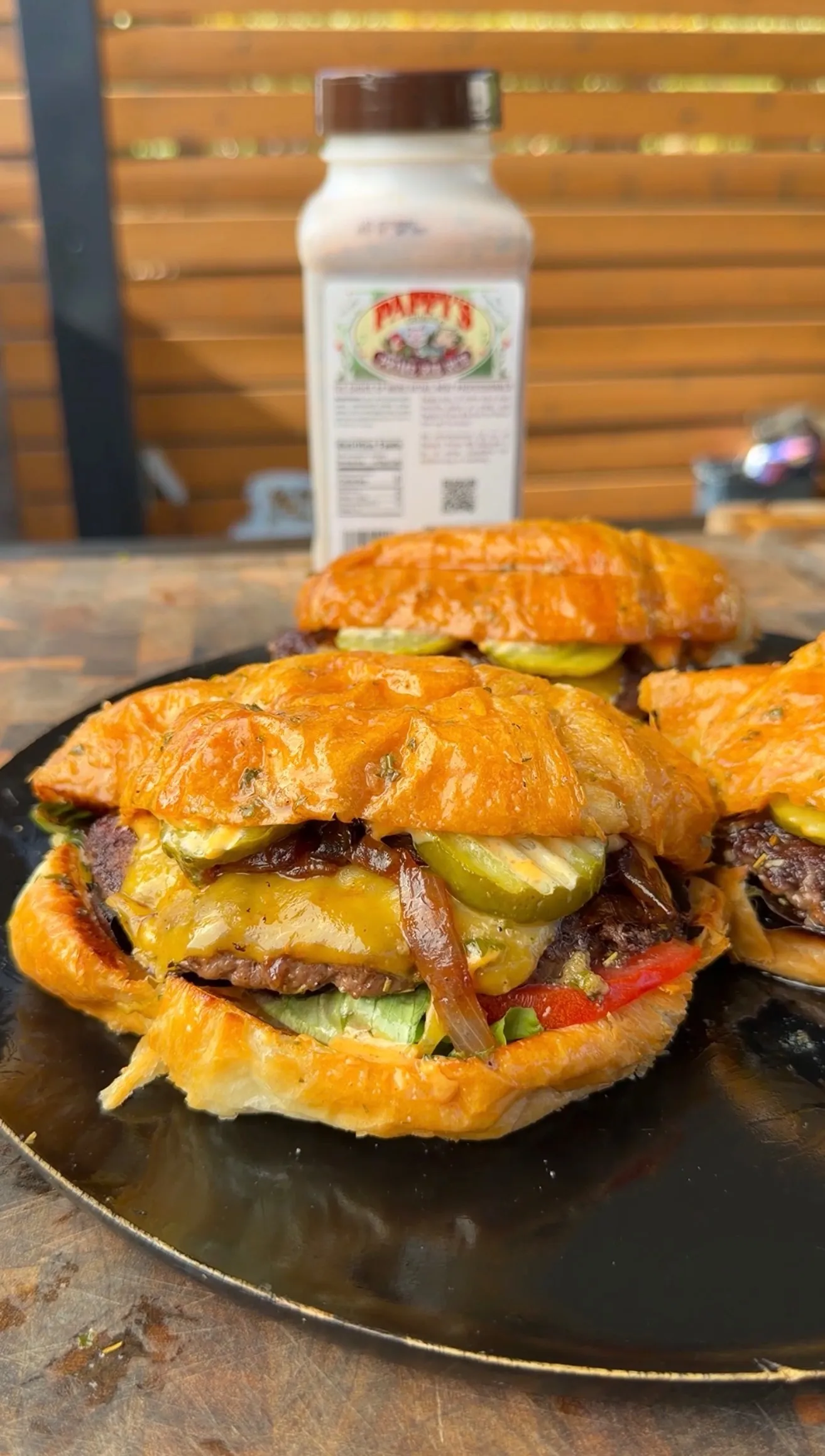 Juicy croissant burgers with melted cheese, pickles, caramelized onions, and fresh veggies on a dark plate