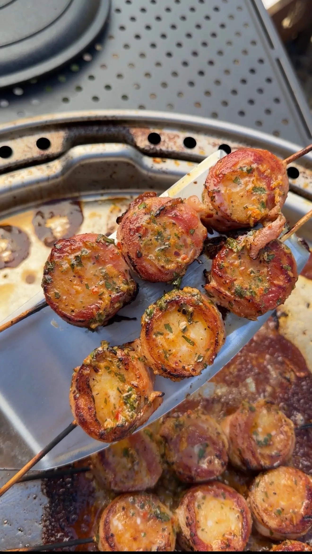 Grilled bacon-wrapped scallops on wooden skewers glazed with cowboy butter herb sauce on a metal grill pan