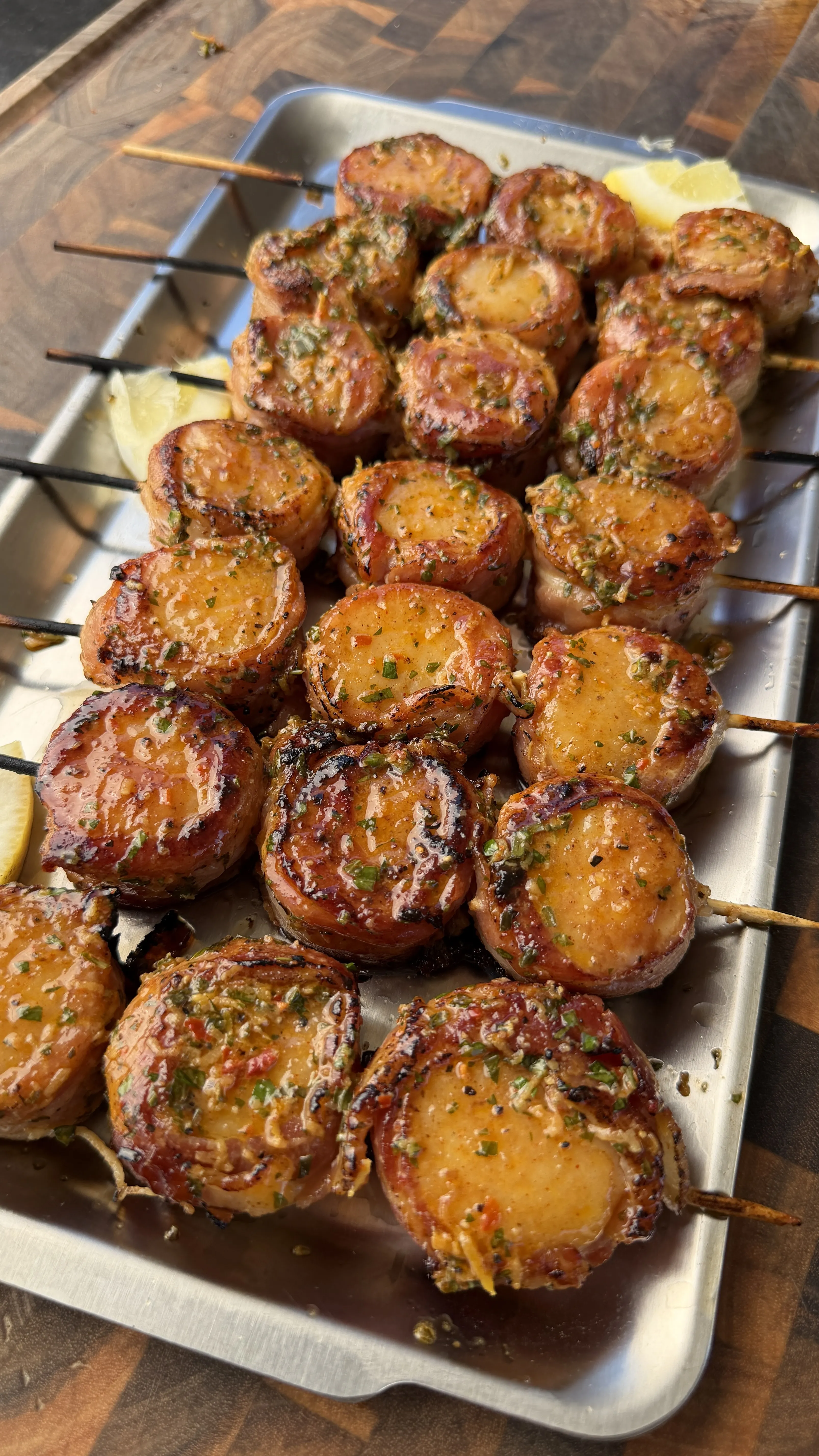 Grilled bacon-wrapped scallops on skewers glazed with cowboy butter herb sauce on a metal tray
