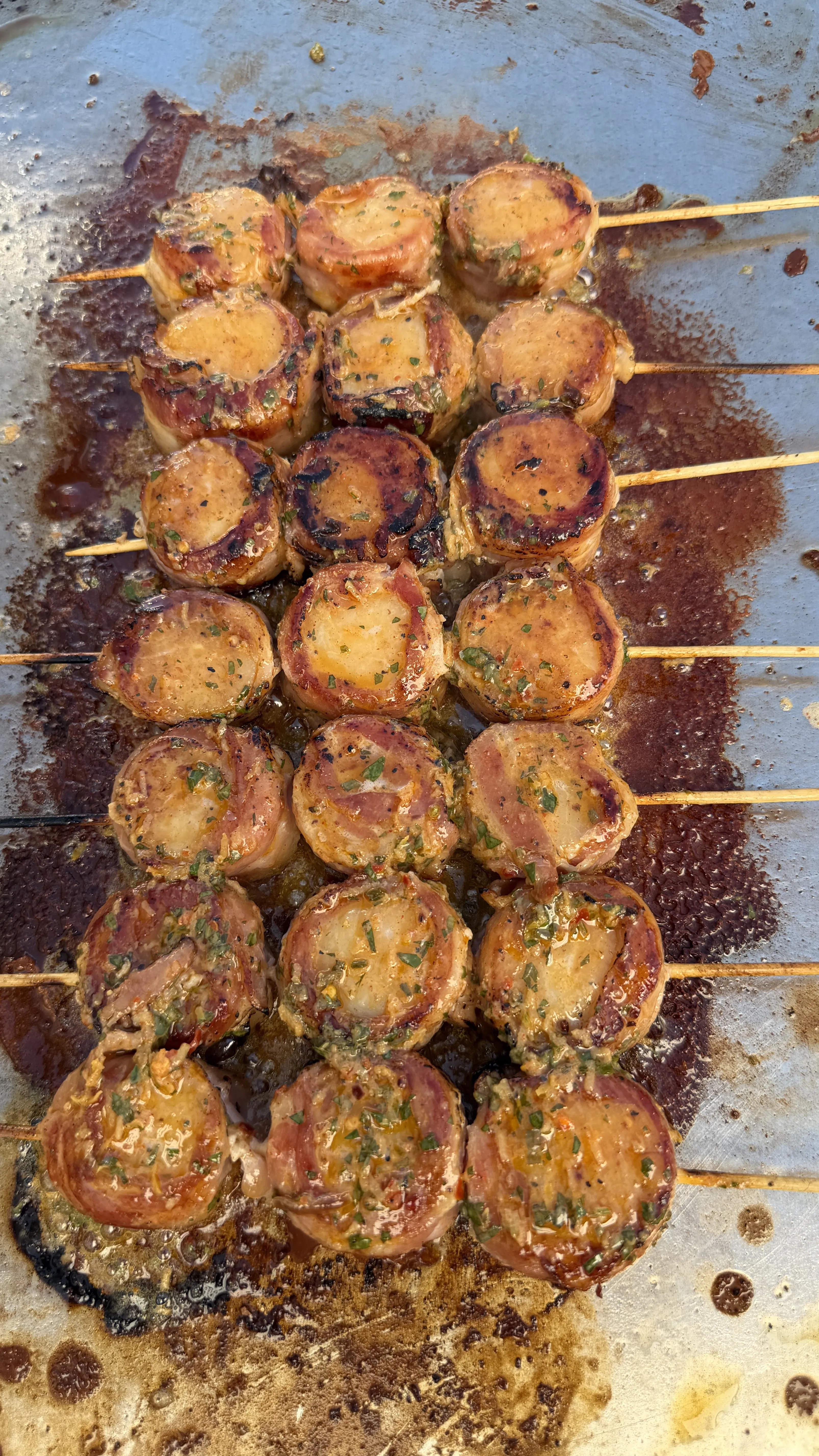 Grilled cowboy butter bacon-wrapped scallop skewers glazed and golden on a metal tray