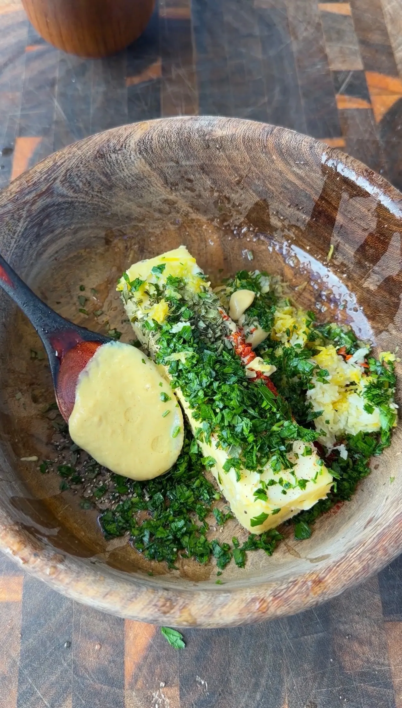 Cowboy butter mixture with fresh herbs, garlic, mustard, and lemon zest in a rustic wooden bowl