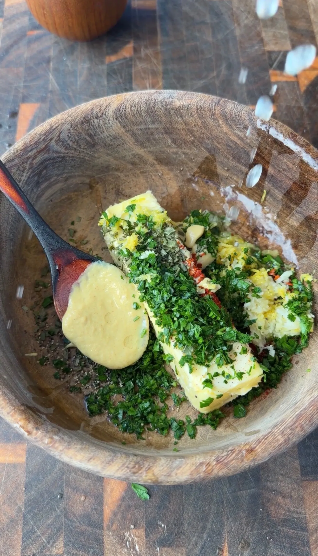 Cowboy butter ingredients in a wooden bowl with chopped parsley, garlic, mustard, and spices being mixed with a wooden spoon