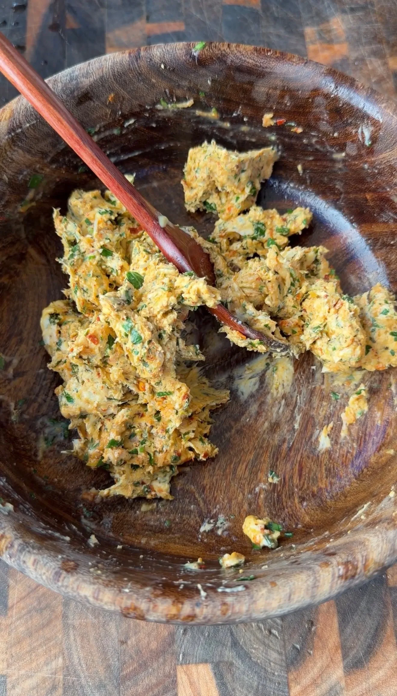 Herbed cowboy butter mixture with fresh herbs and spices being mixed in a rustic wooden bowl