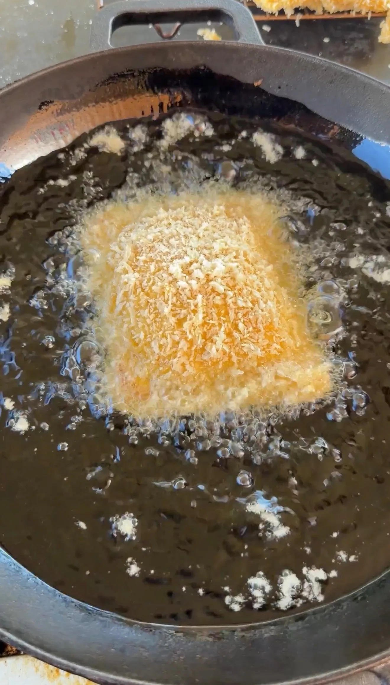 Breaded cheesesteak stuffed pocket frying in hot oil in a cast iron skillet with golden panko crust