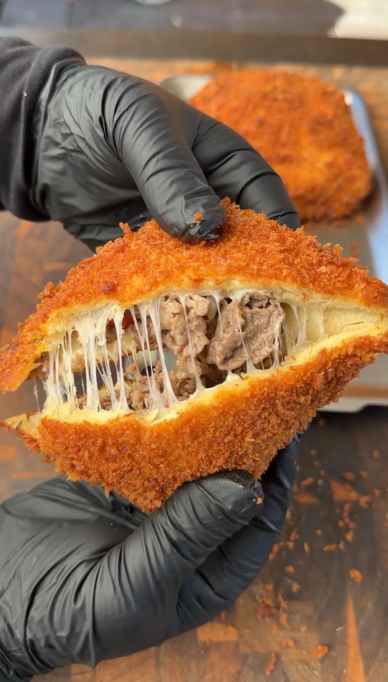 Hands pulling apart a crispy breaded cheesesteak pocket revealing melted cheese and seasoned beef filling