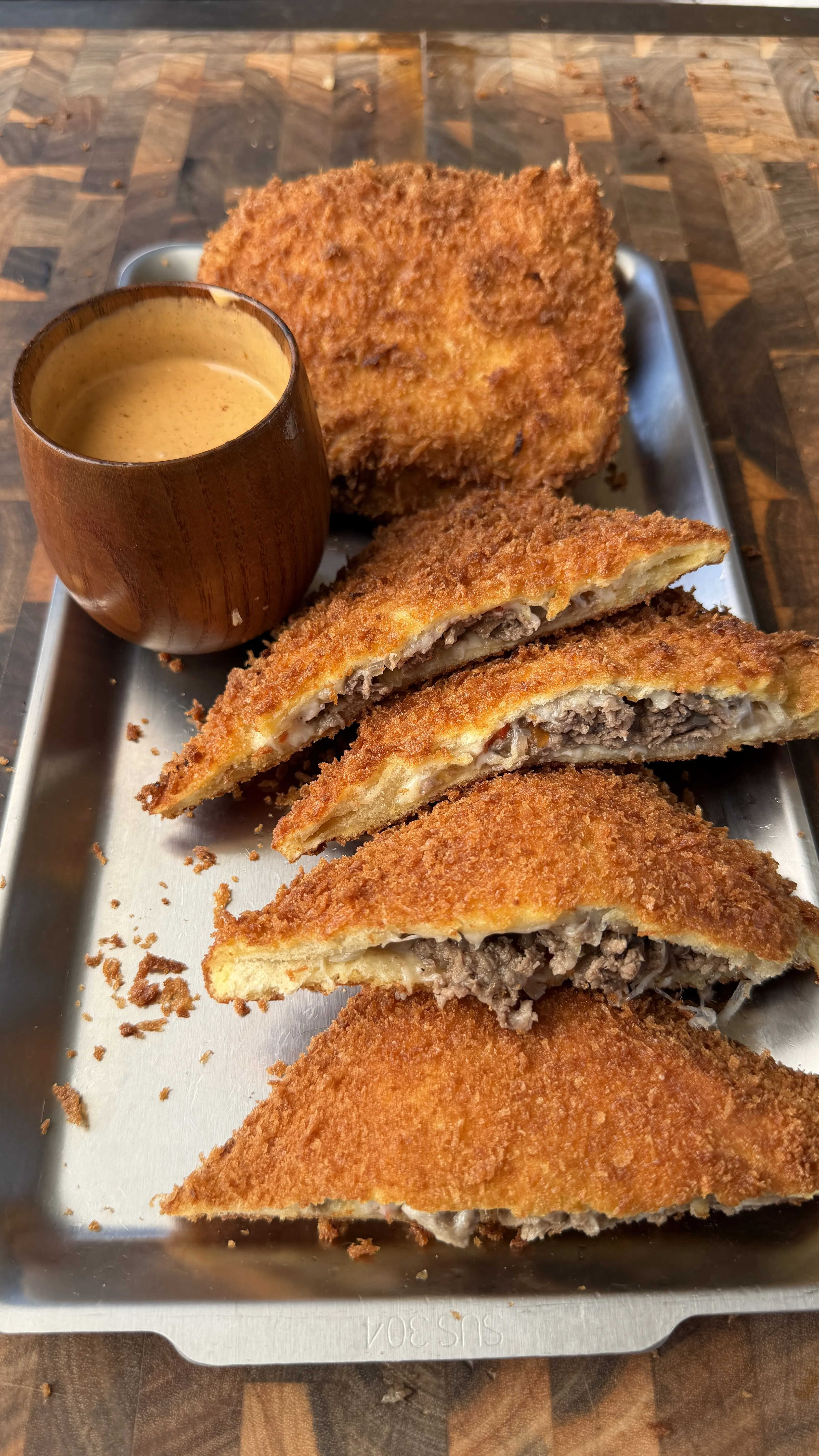 Golden panko-crusted cheesesteak stuffed pockets sliced open on a metal tray with dipping sauce
