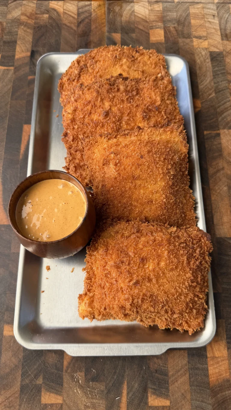 Four golden crispy panko-breaded cheesesteak stuffed pockets on a metal tray with creamy dipping sauce