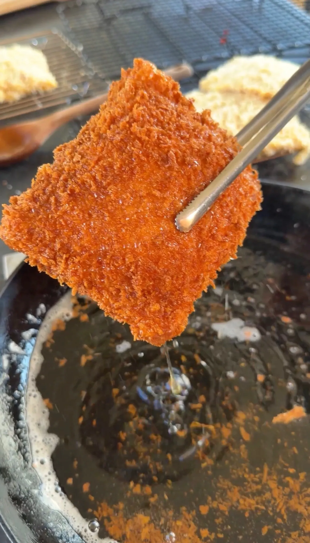 Golden-orange crispy cheesesteak stuffed pocket held with metal tongs over hot frying oil, dripping excess oil