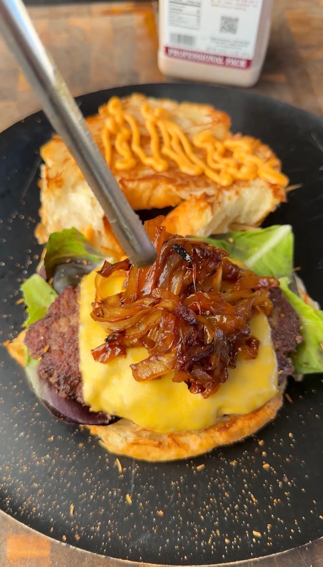 Croissant burger with melted cheese, caramelized onions, and lettuce on a dark plate