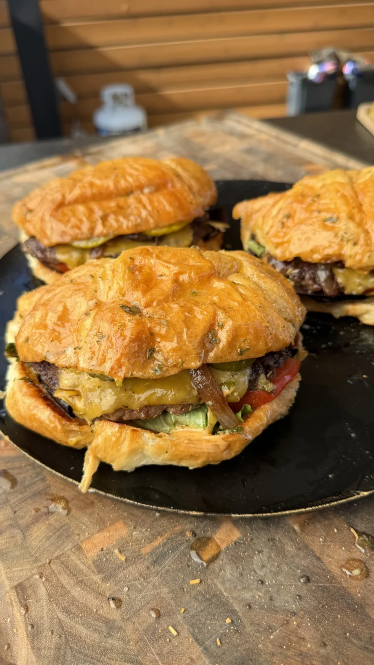 Juicy croissant burgers with melted cheese, pickles, tomato, and caramelized onions served on a black plate