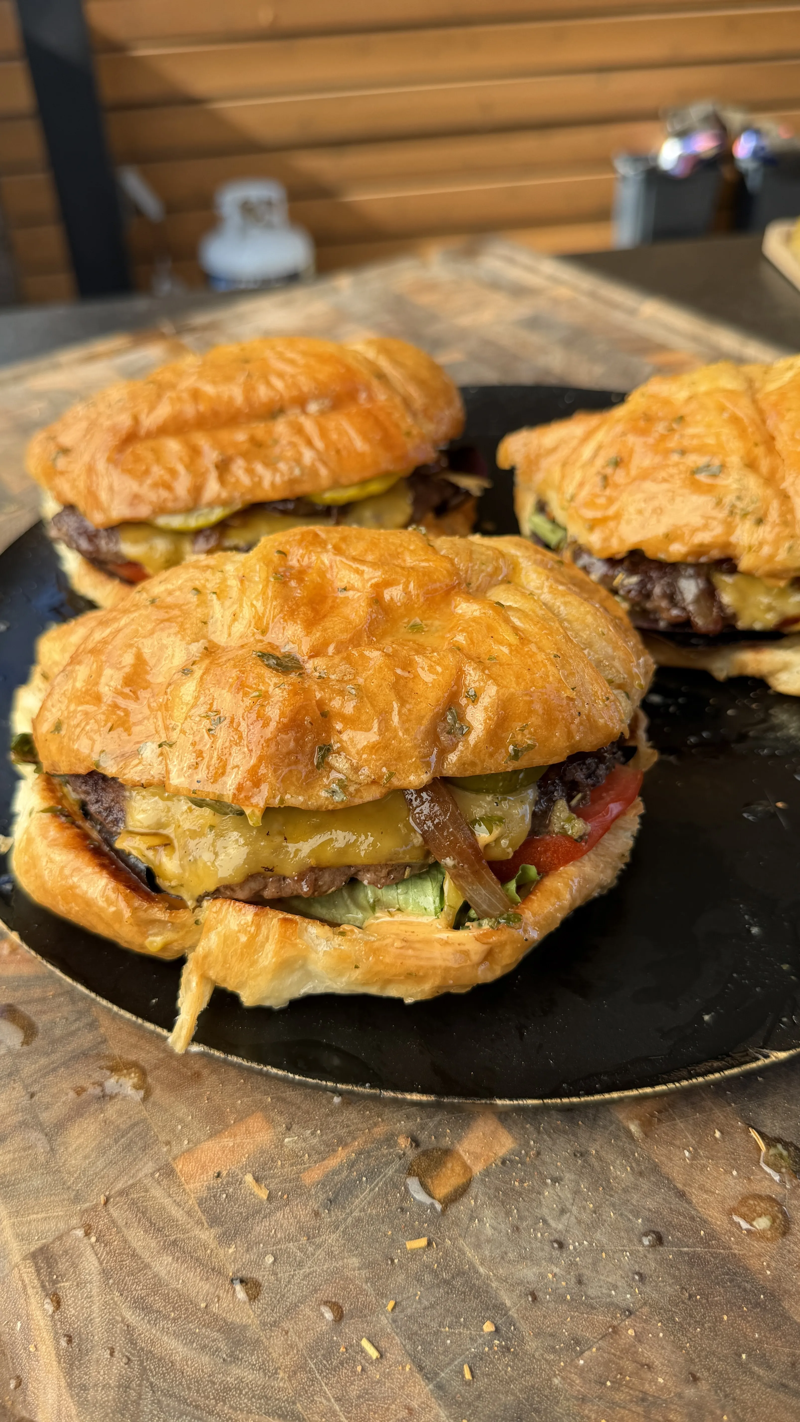Juicy croissant burgers with melted cheese, pickles, tomato, and caramelized onions served on a black plate