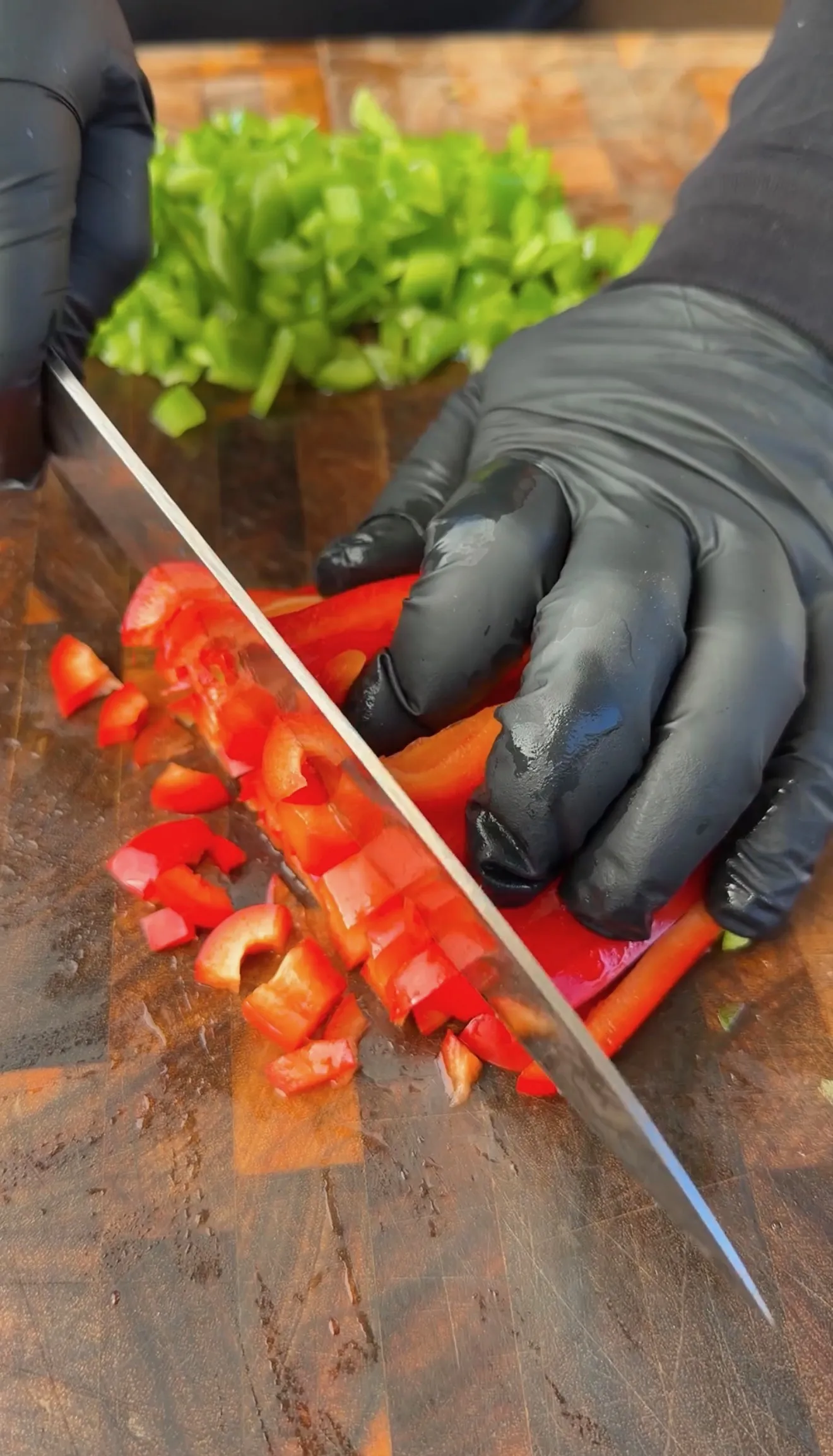 Hands in black gloves dicing red bell pepper on a wooden cutting board for breakfast skillet