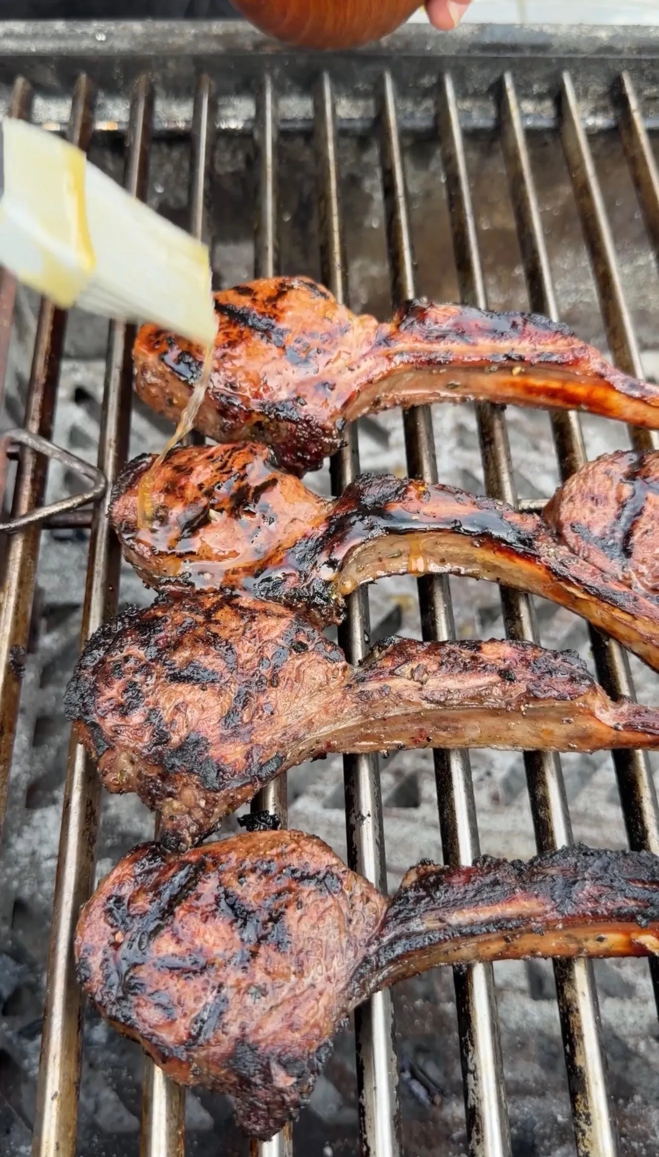 Lamb lollipop chops grilling over charcoal being basted with sauce using a pastry brush