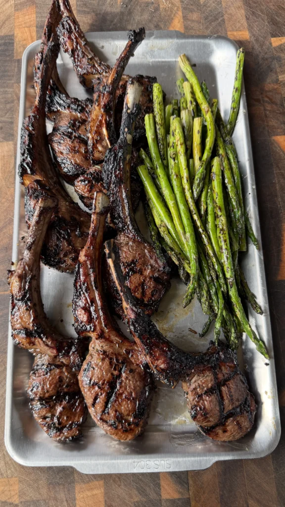 Grilled garlic and sherry lamb lollipop chops with charred asparagus on a stainless steel tray