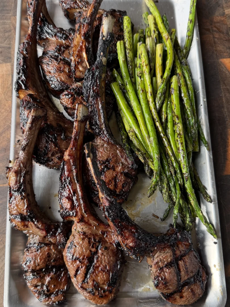 Grilled garlic and sherry lamb lollipop chops with charred asparagus on a stainless steel tray