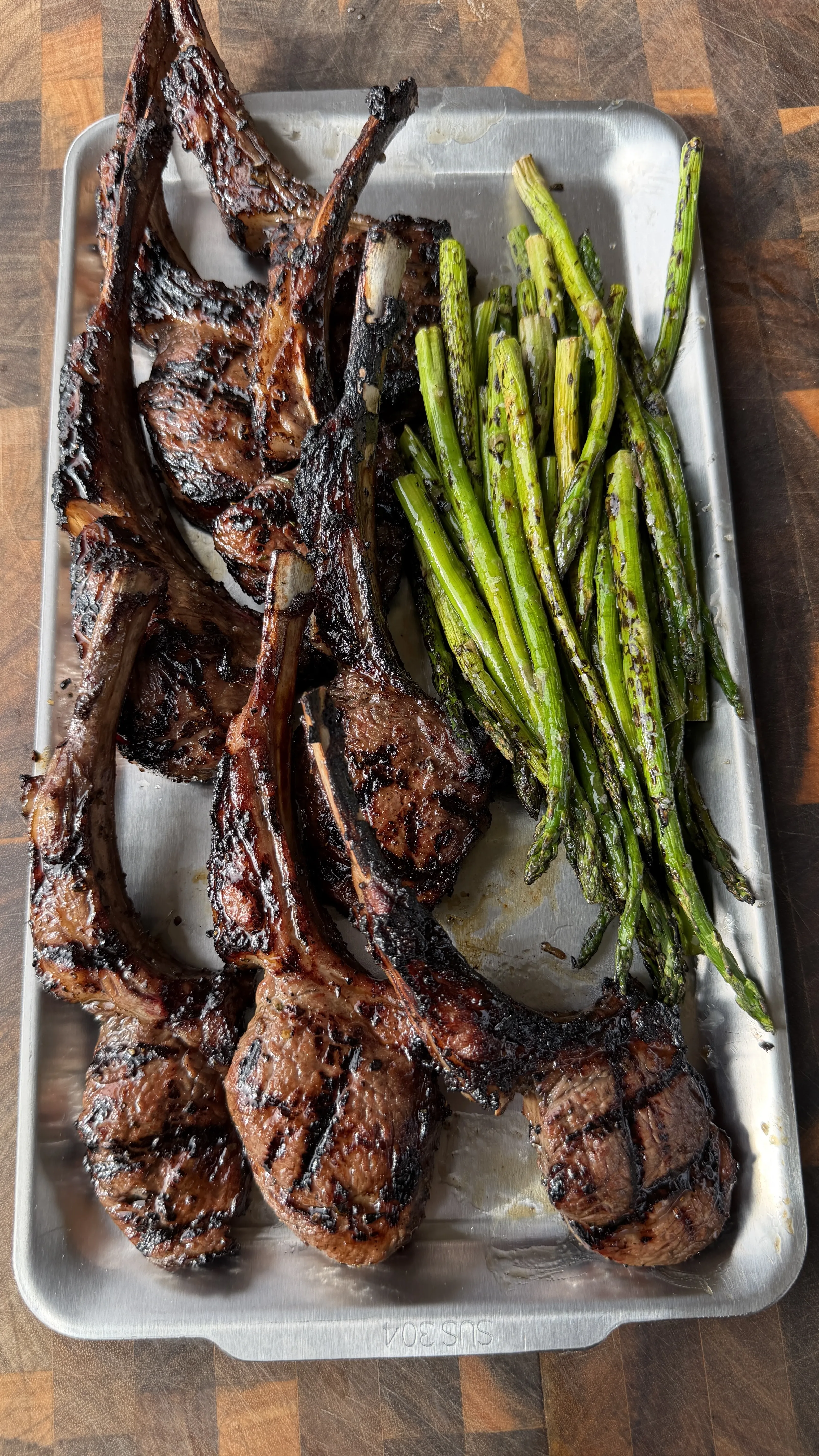 Grilled garlic and sherry lamb lollipop chops with charred asparagus on a stainless steel tray