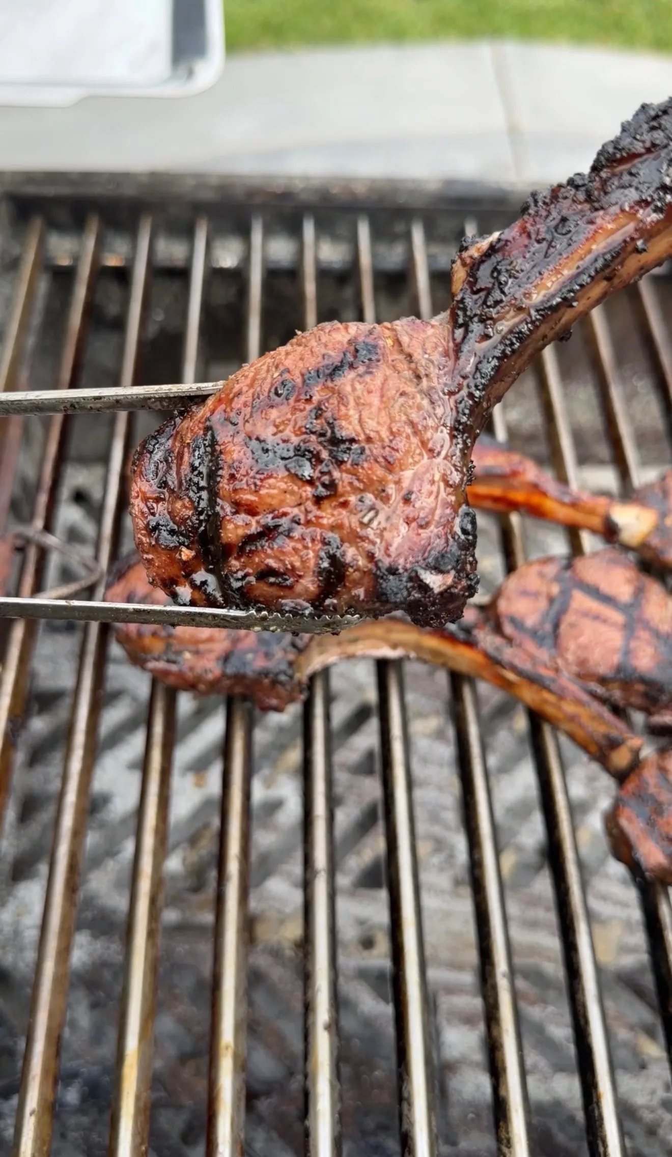 Lamb lollipop chops with a caramelized garlic sherry glaze being turned on a hot outdoor grill with tongs