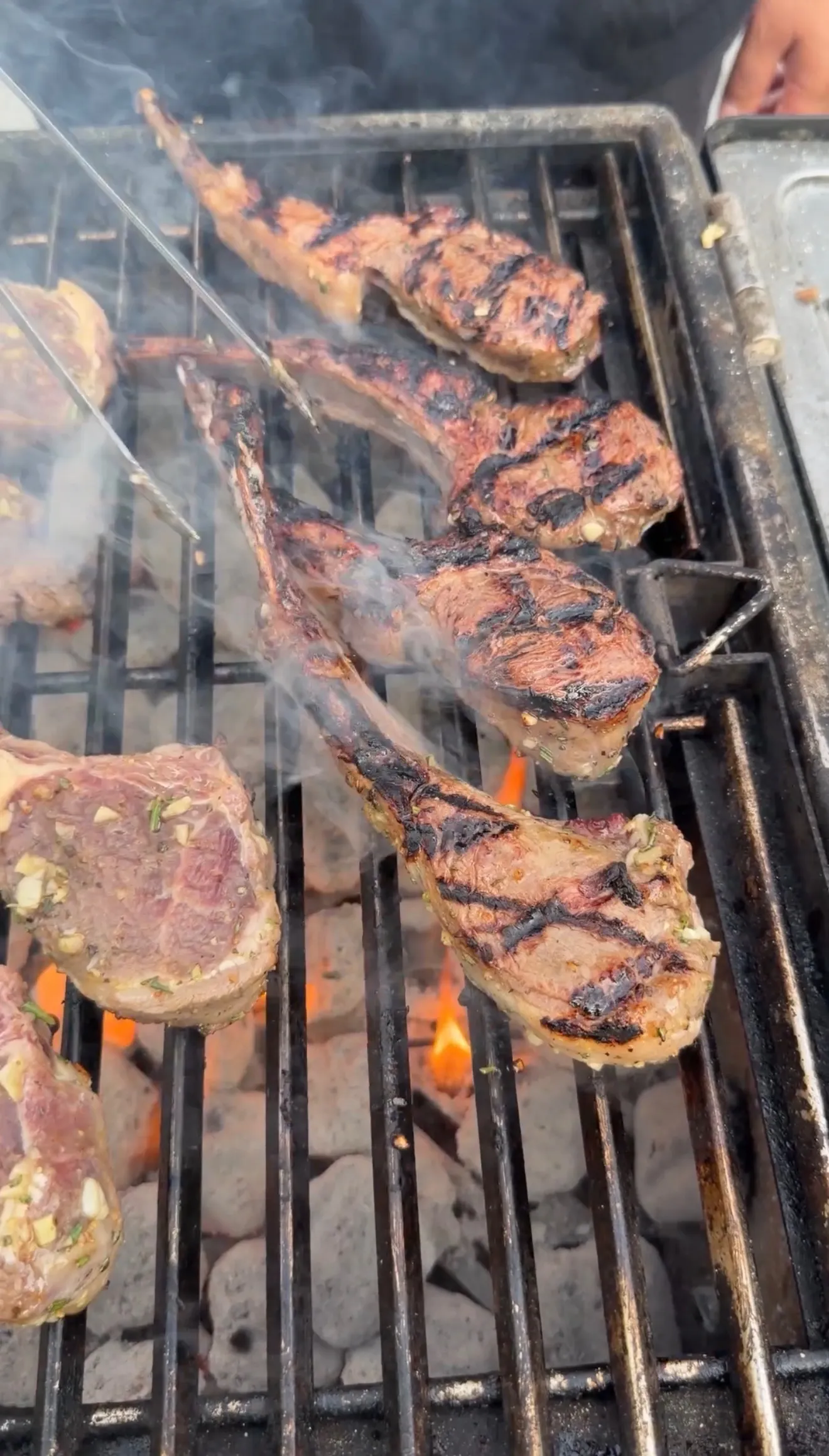 Garlic and sherry marinated lamb lollipop chops grilling over open flames with char marks and rising smoke