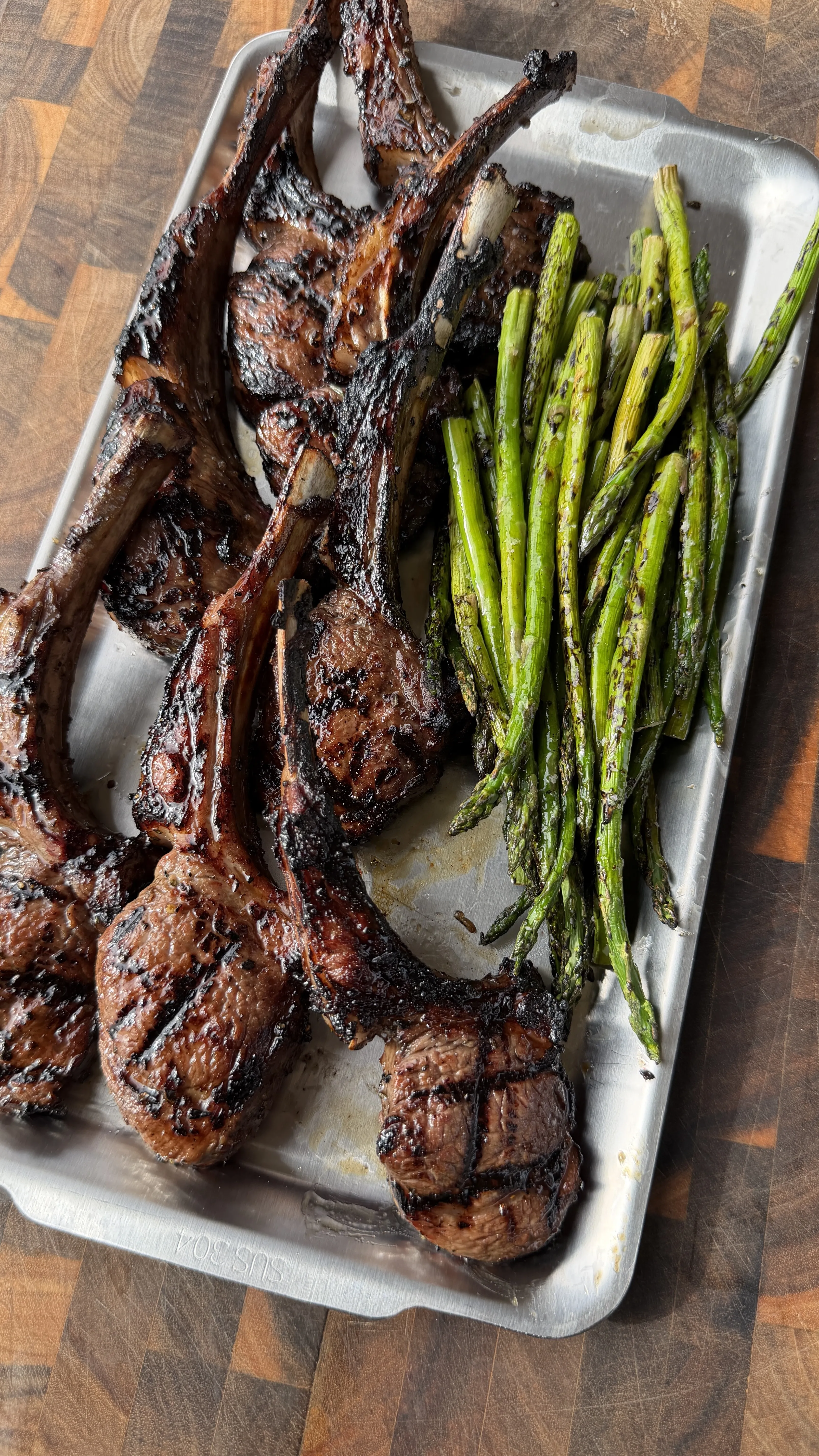 Grilled garlic sherry lamb lollipops plated with charred asparagus on a serving tray