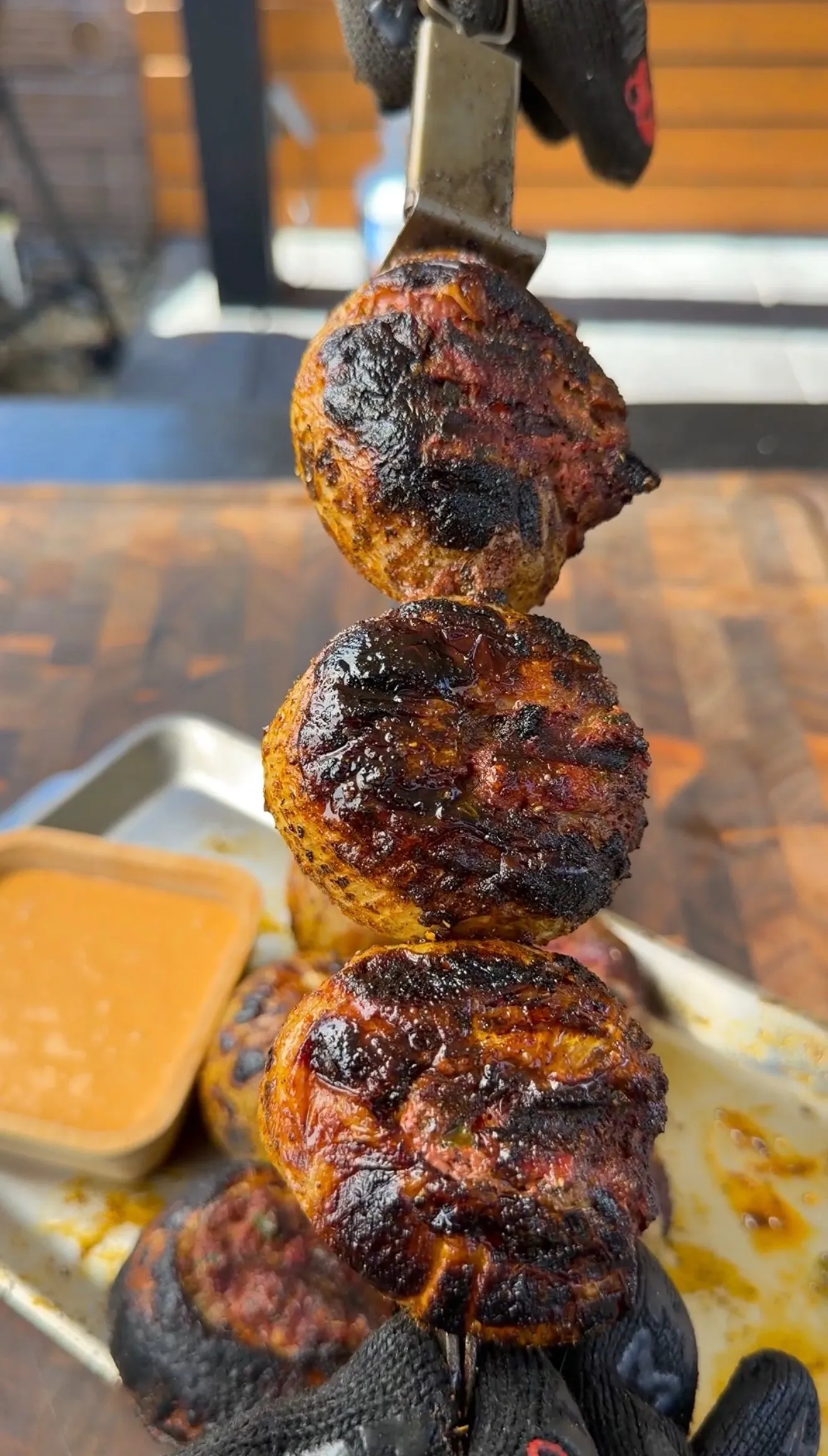 Four charred stuffed onion bombs skewered on a metal rod, held over a tray with dipping sauce
