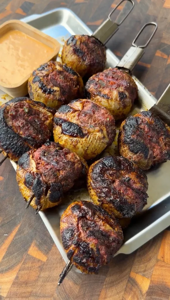 Charred stuffed onion bombs on metal skewers served on a tray with creamy dipping sauce