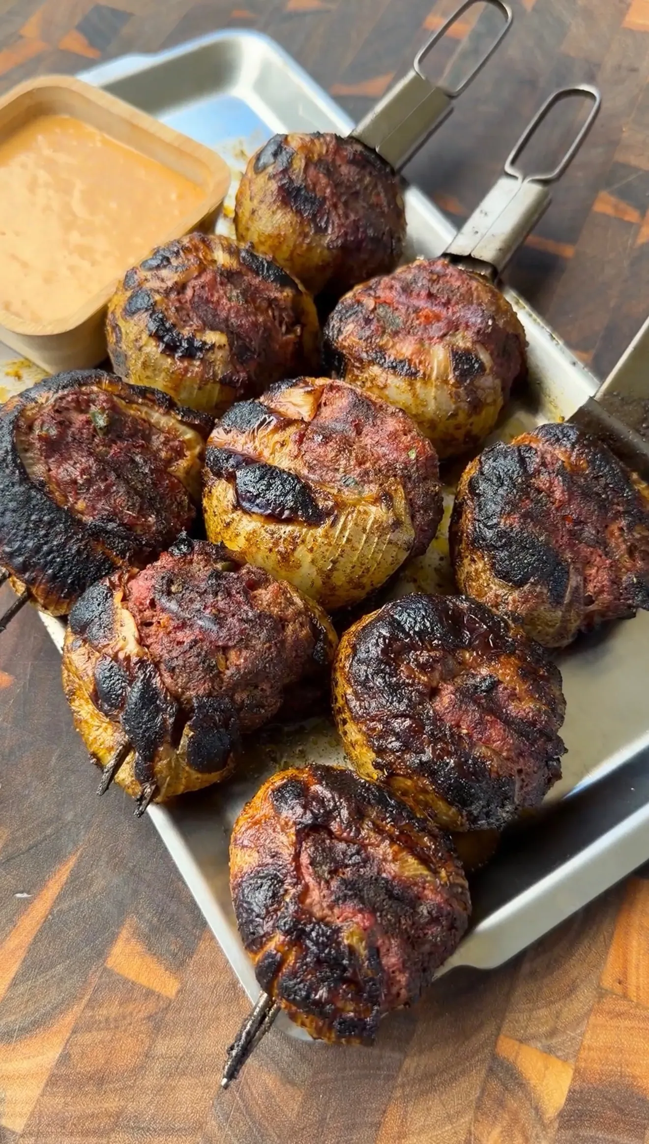Charred stuffed onion bombs on metal skewers served on a tray with creamy dipping sauce