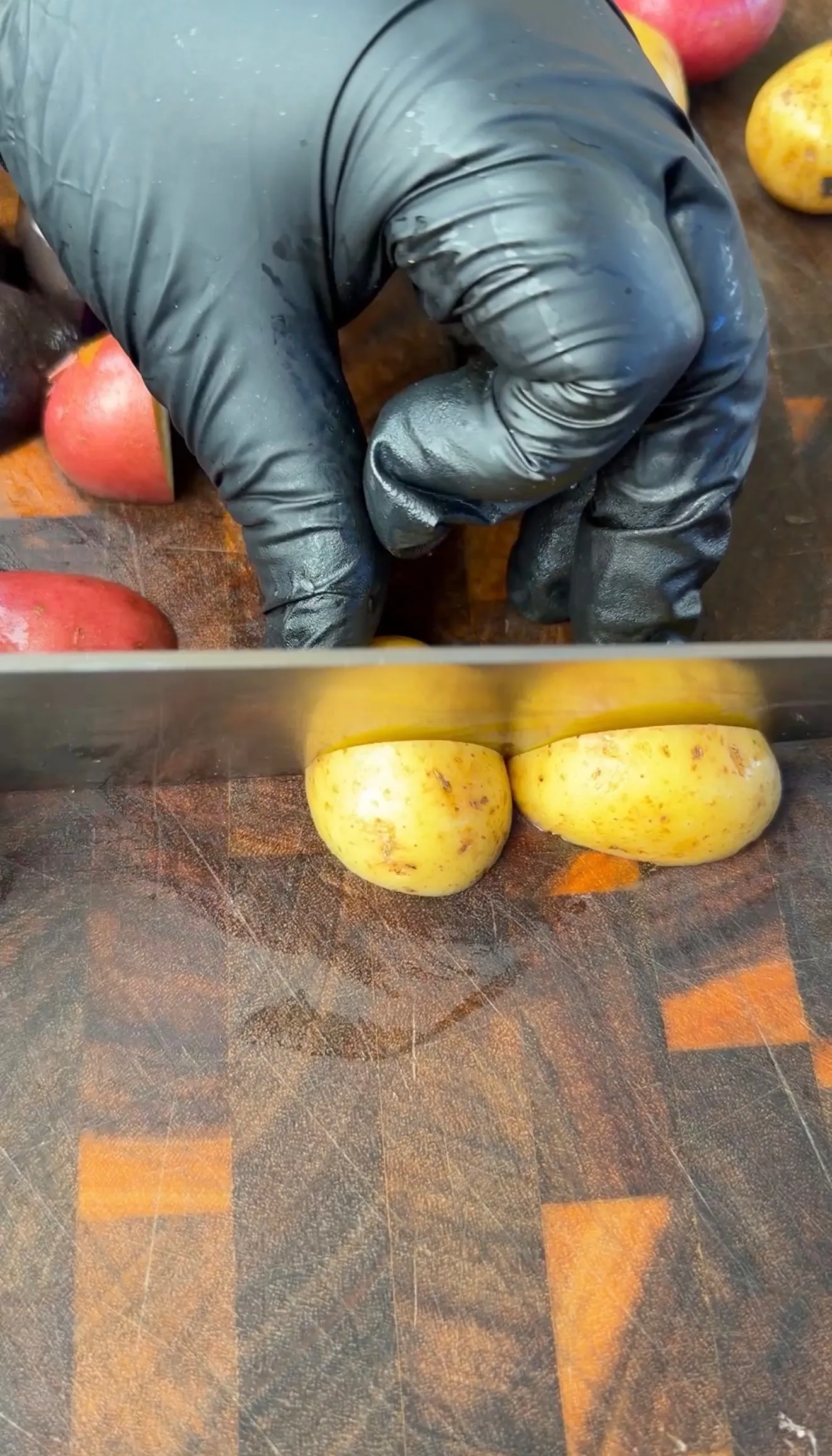 Gloved hands slicing yellow baby potatoes in half on a dark cutting board for breakfast skillet