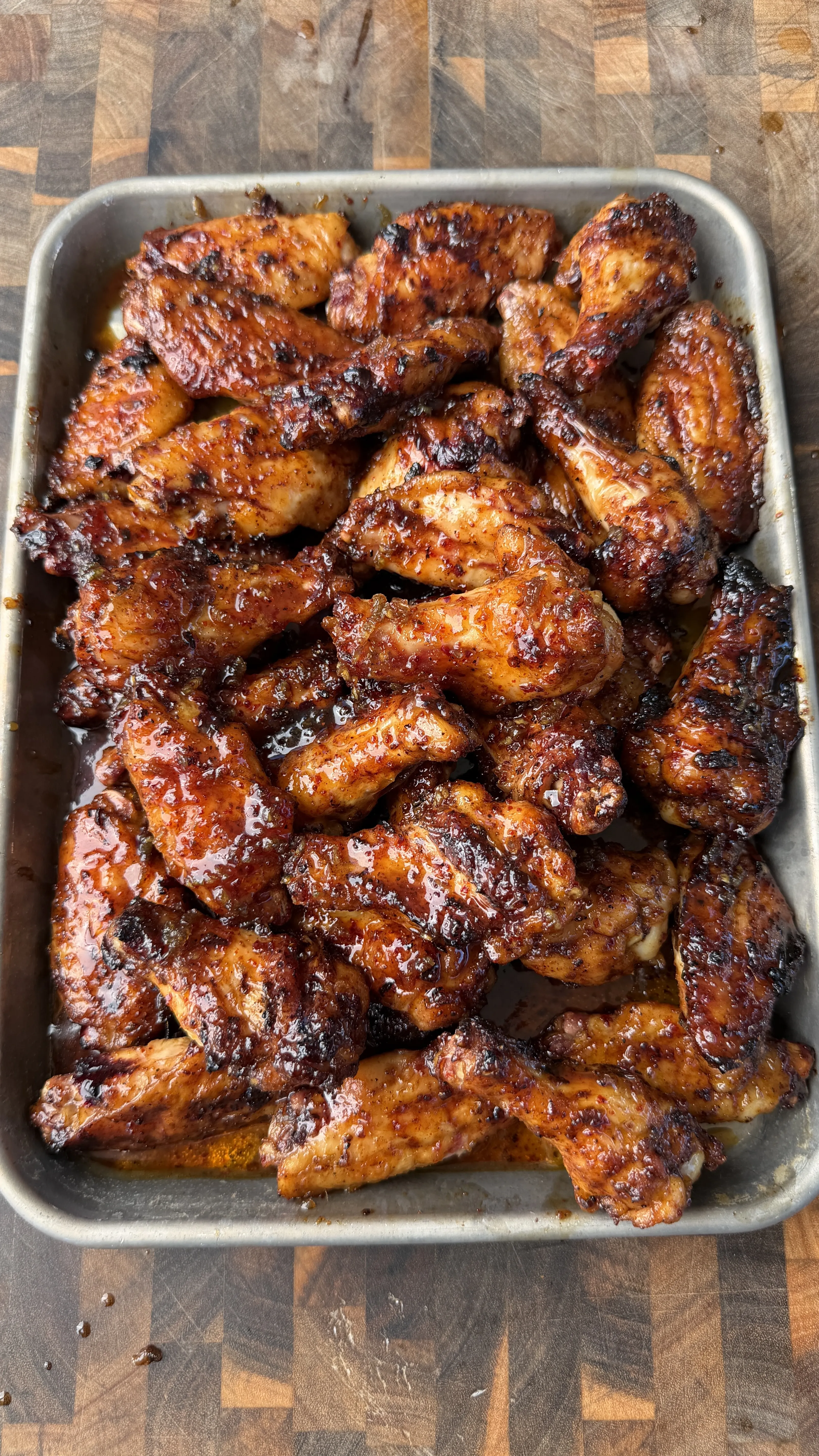 Sticky honey garlic chicken wings piled in a metal baking pan on a wooden cutting board