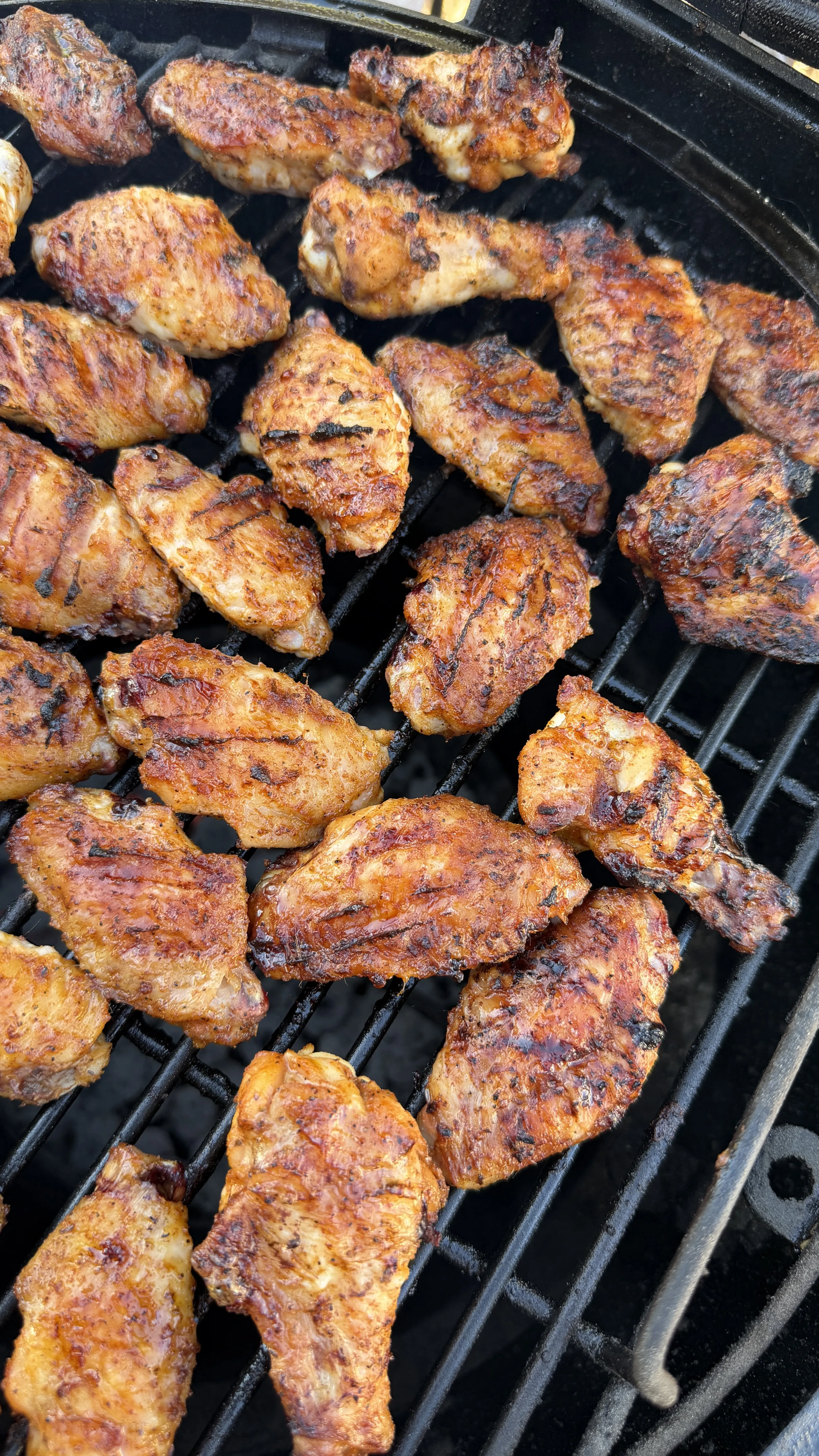 Honey garlic chicken wings with char marks grilling on a round black BBQ grill grate