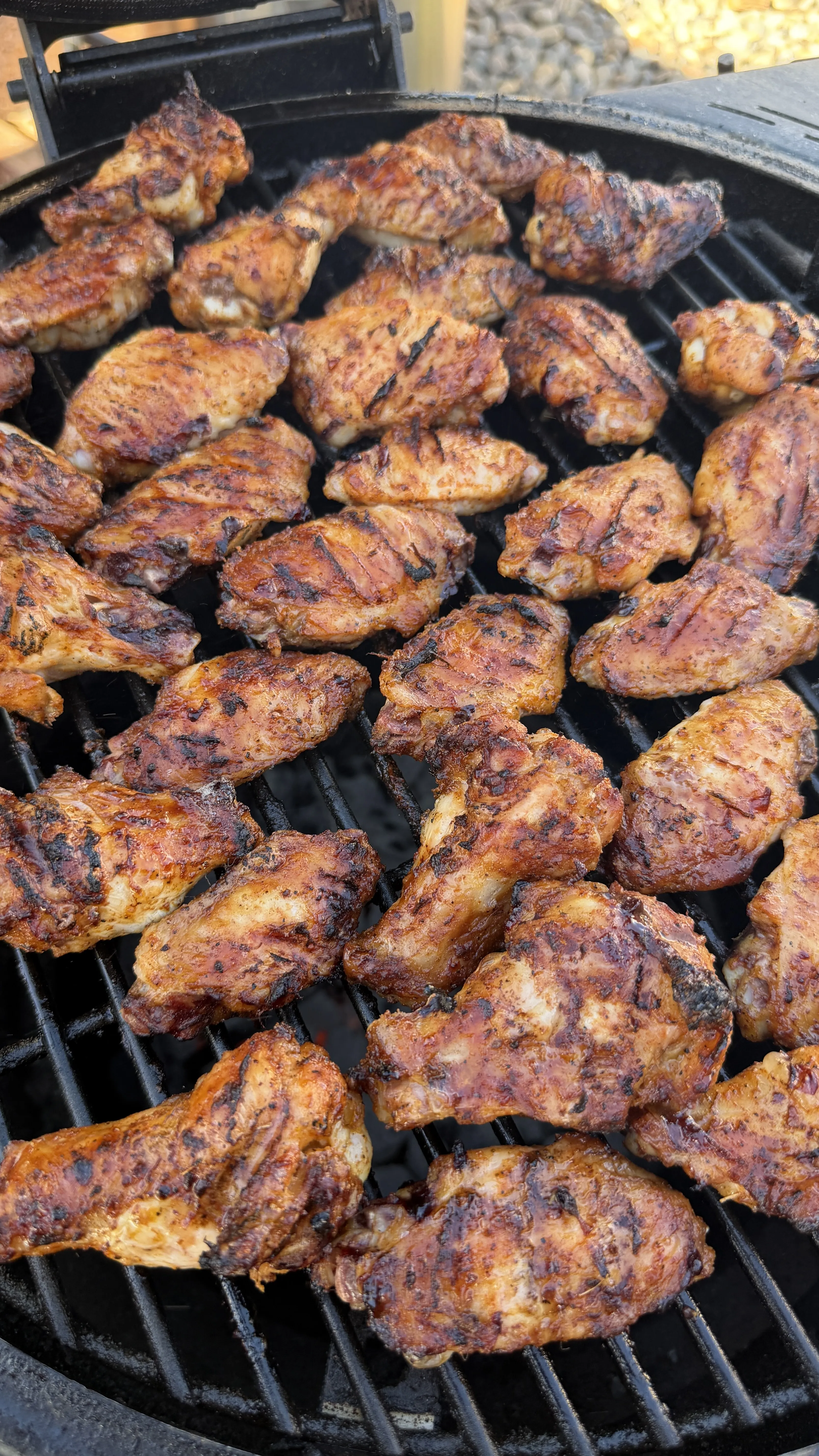 Honey garlic chicken wings with grill marks cooking on a round charcoal grill, golden-brown and caramelized