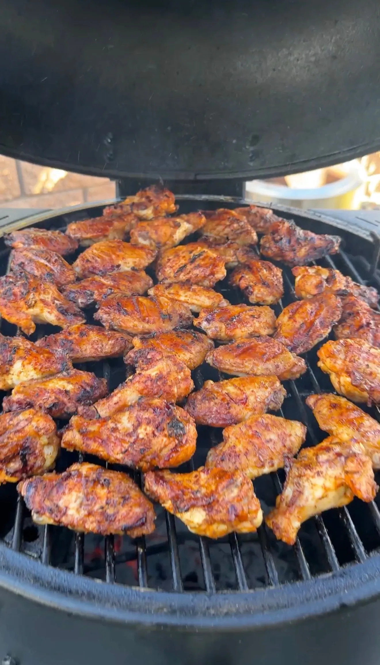 Dozens of glazed honey garlic chicken wings grilling on a round charcoal grill with caramelized edges