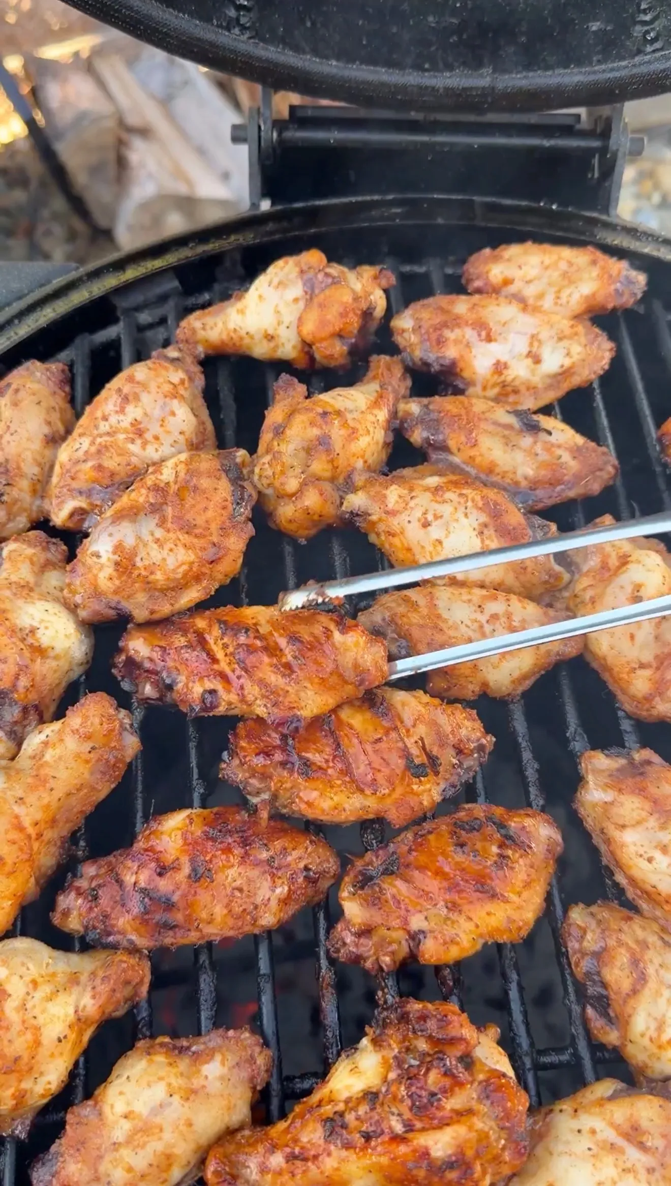 Seasoned honey garlic chicken wings grilling on a charcoal grill, being turned with tongs