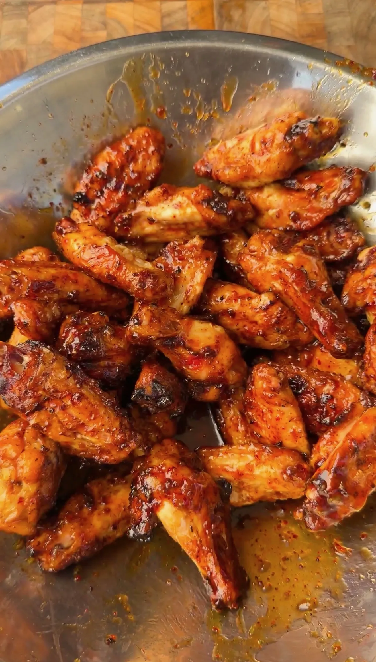 Glazed honey garlic chicken wings piled in a stainless steel bowl with caramelized sauce